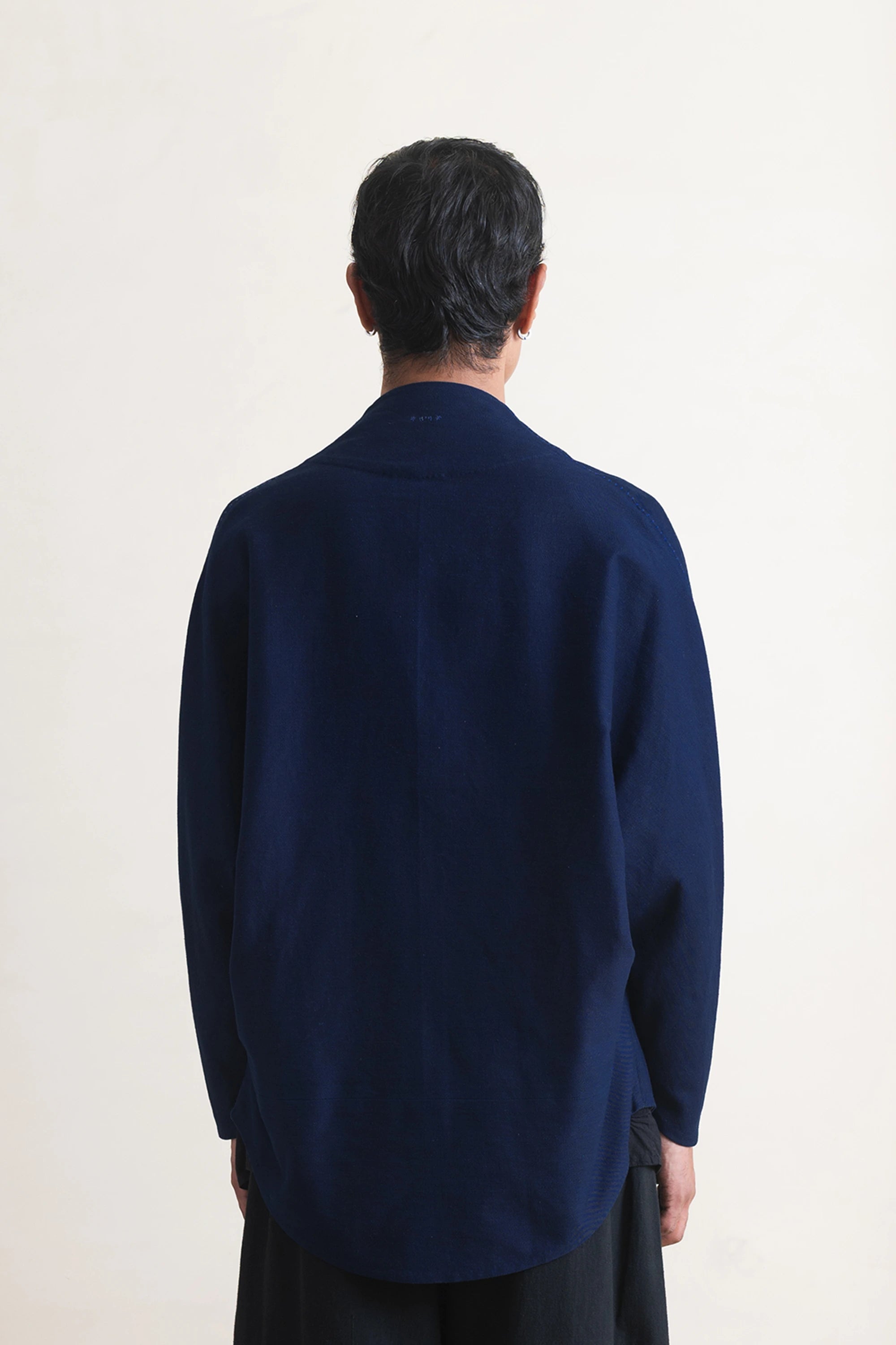 Back shot of a person wearing a indigo coat against a light grey background