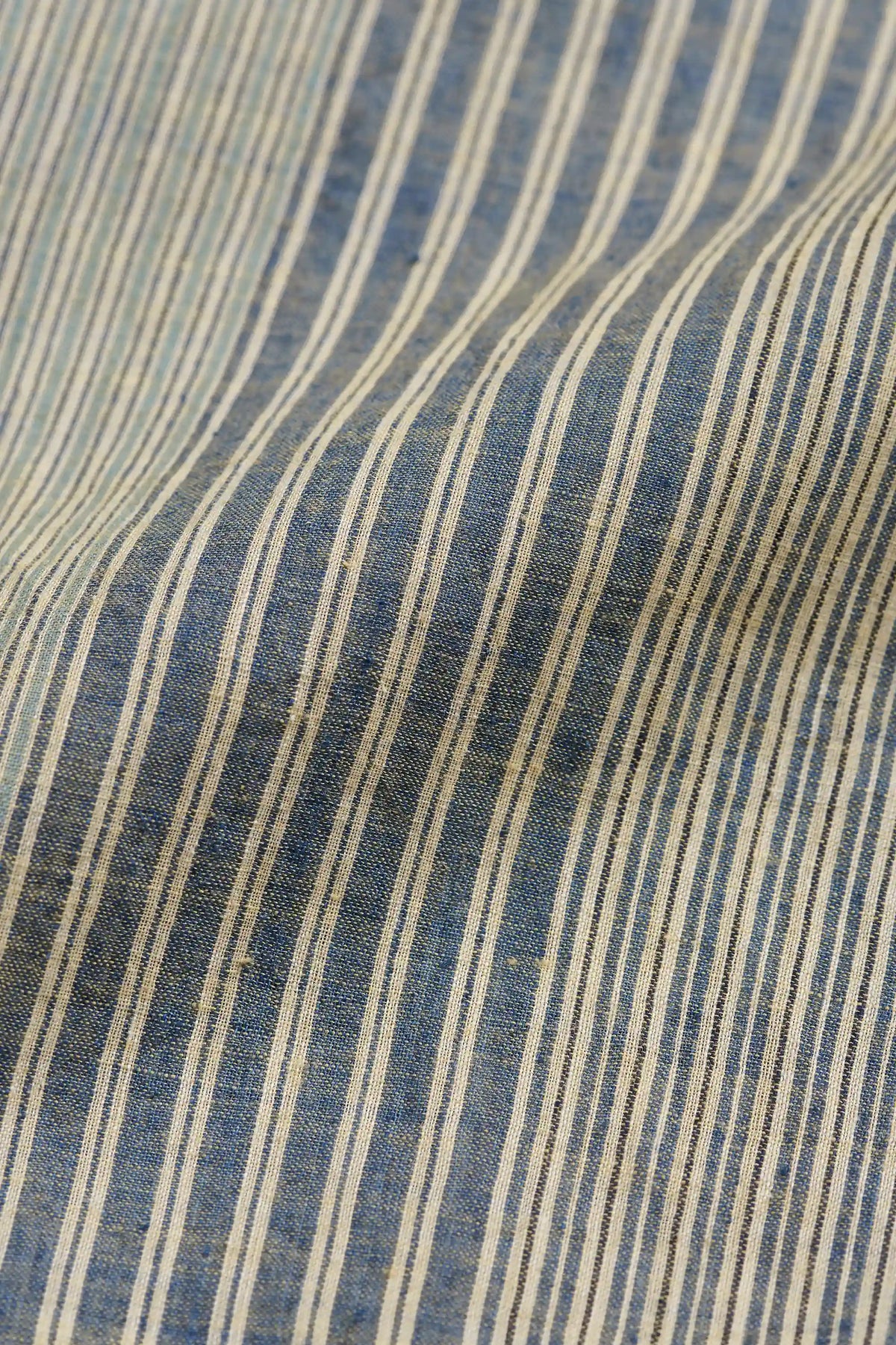 A close-up of a striped fabric with vertical blue and beige stripes, showing a textured woven material with soft folds.