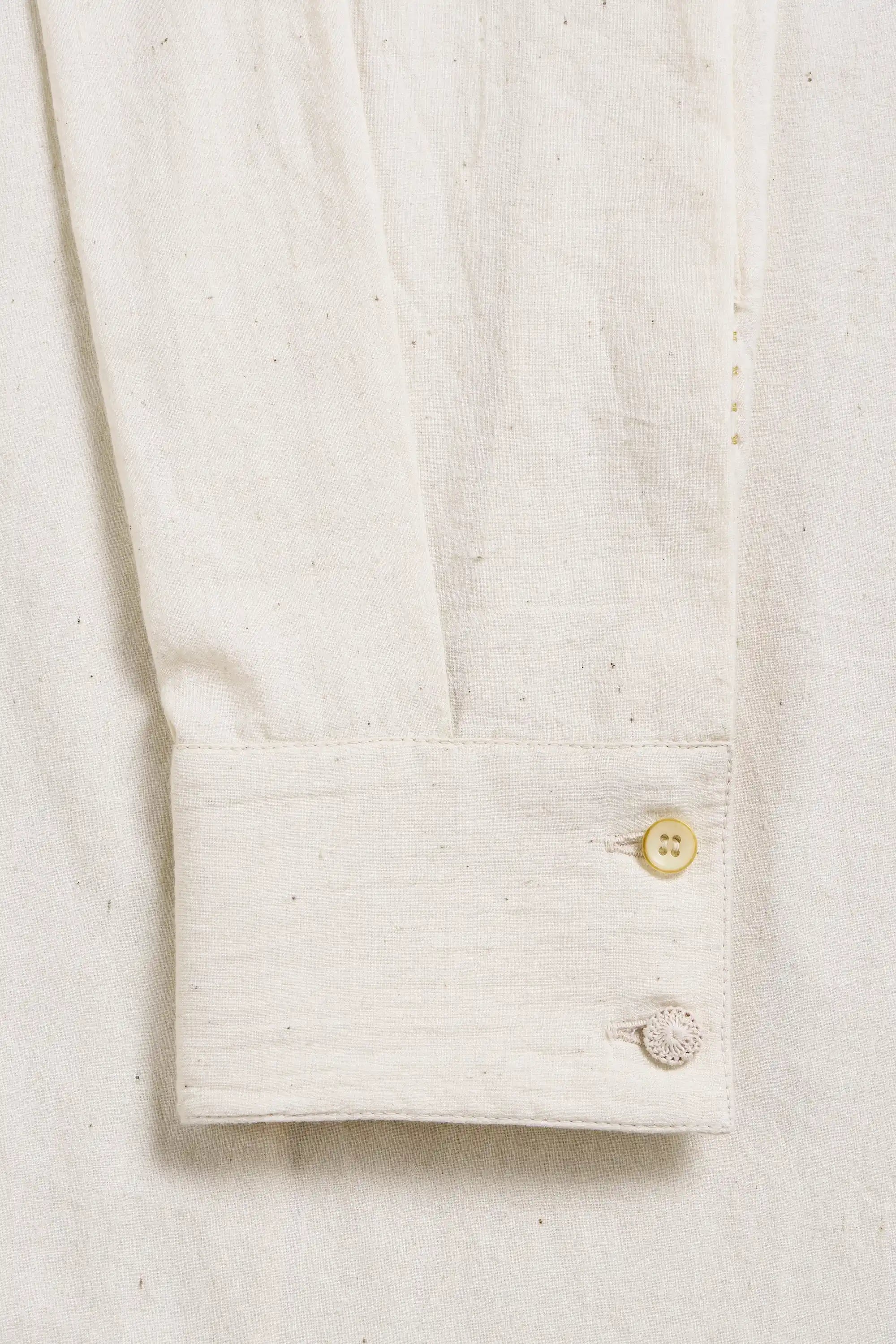Close-up of a ecru shirt with a button and sleeve on a light grey background