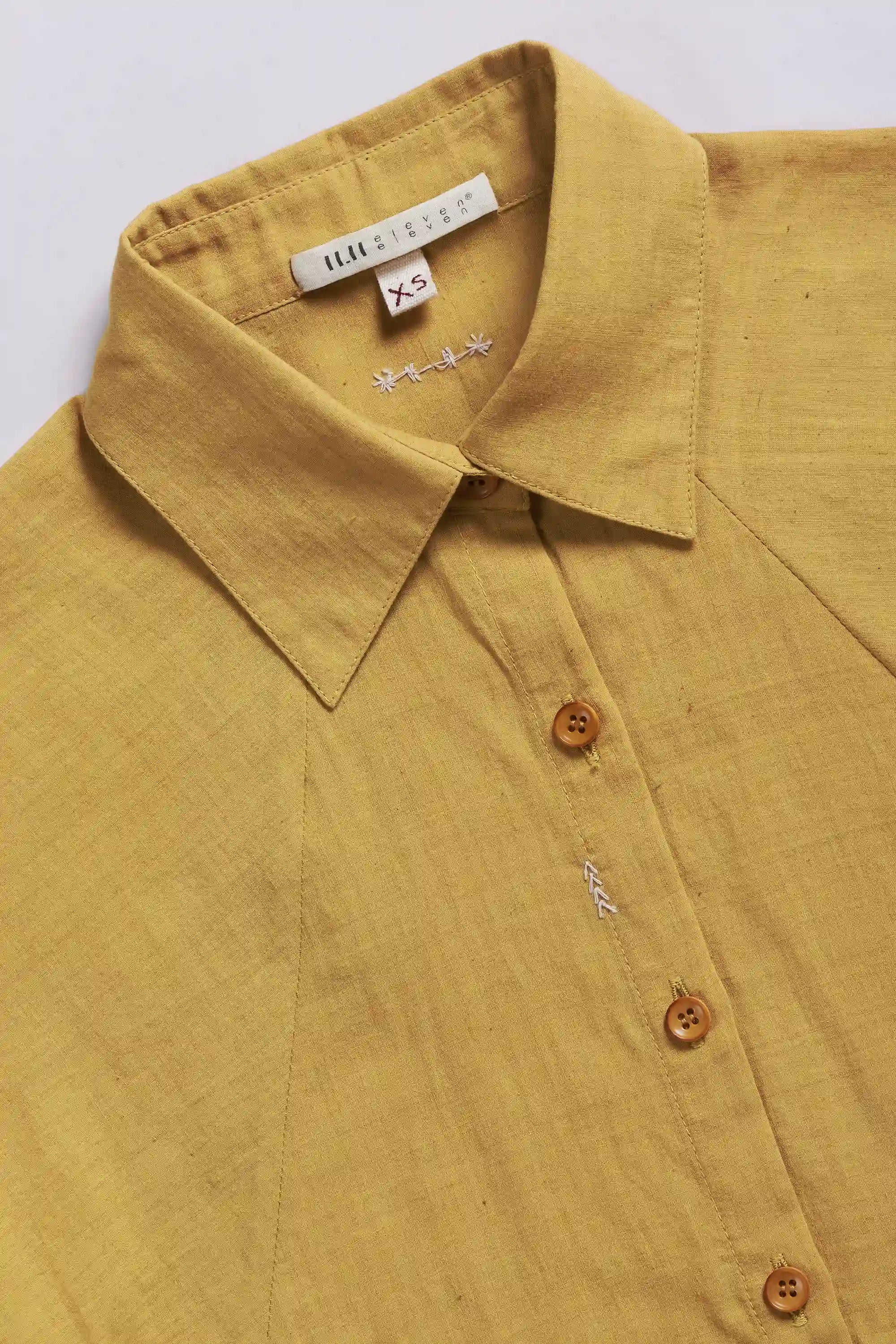 Close-up of a ochre yellow shirt with a collar and buttons, with a brand tag