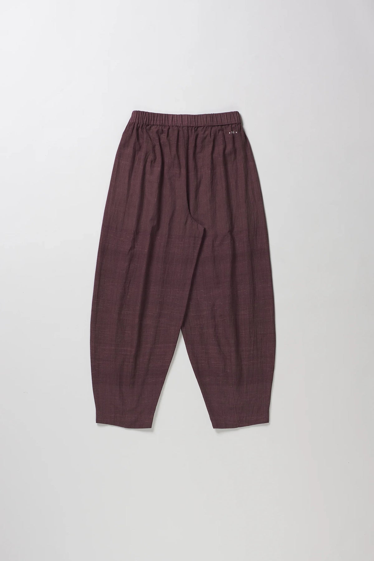 A pair of loose-fitting, pleated trousers in burgundy color, laid flat against a light grey background.