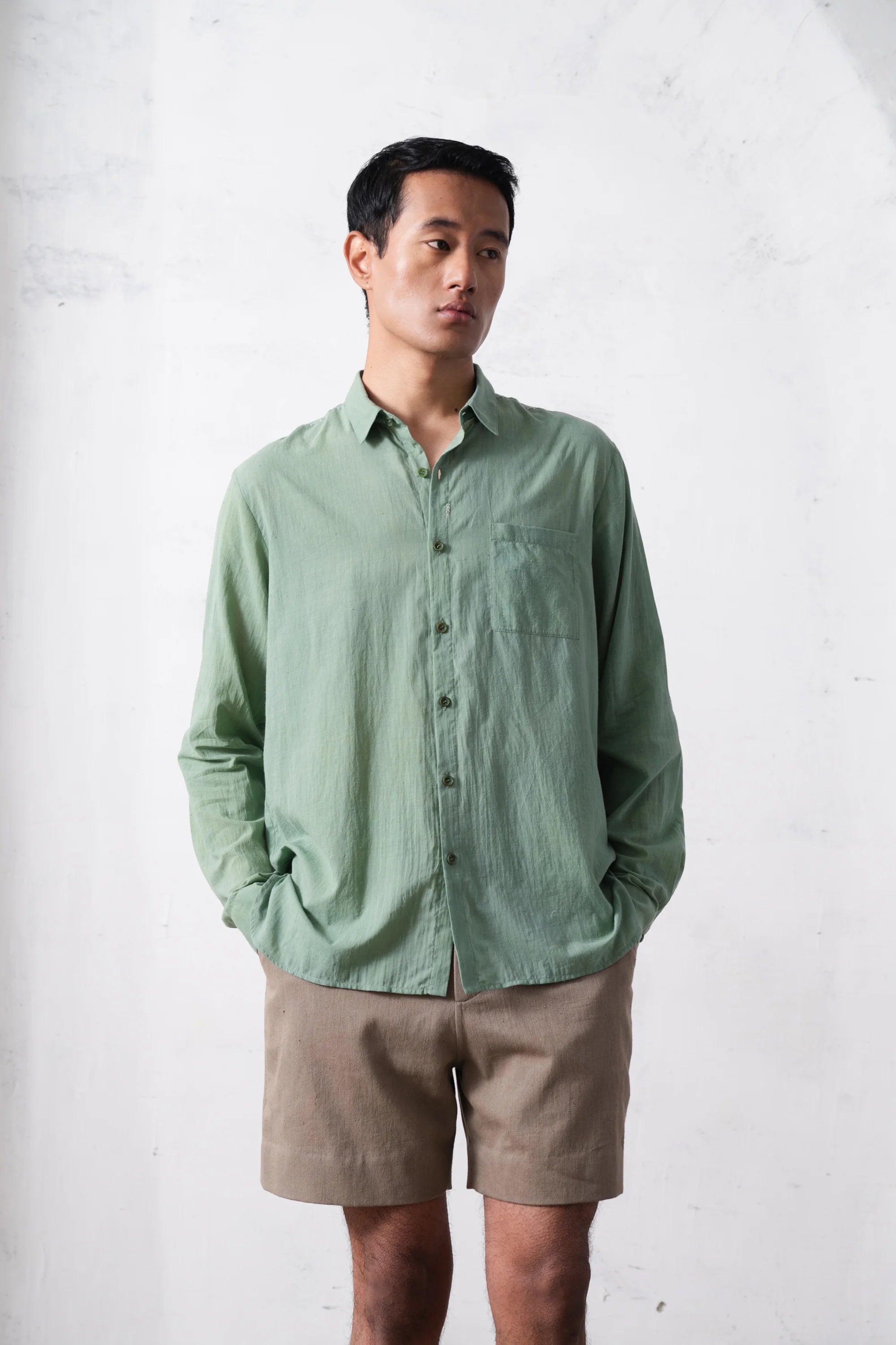 Man wearing a green shirt and beige shorts against a light grey background