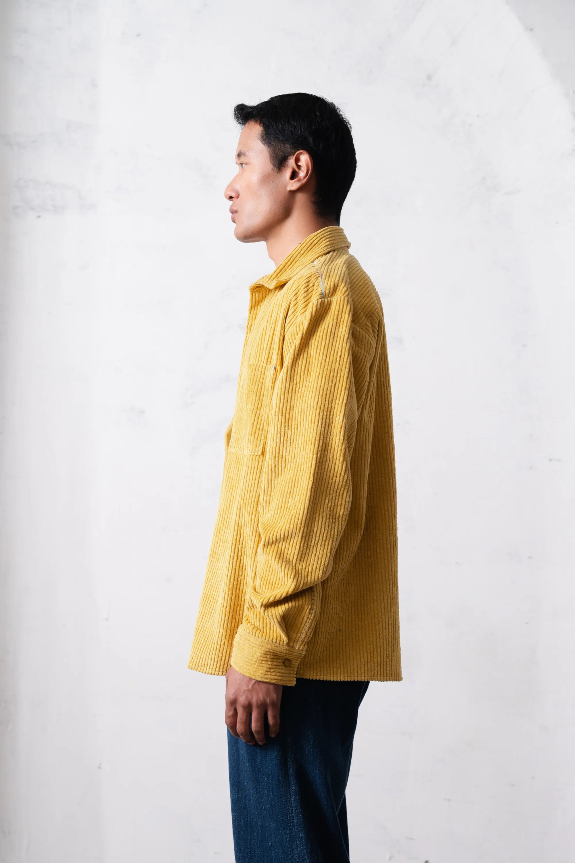 A side shot of a person wearing a yellow shirt against a light grey background