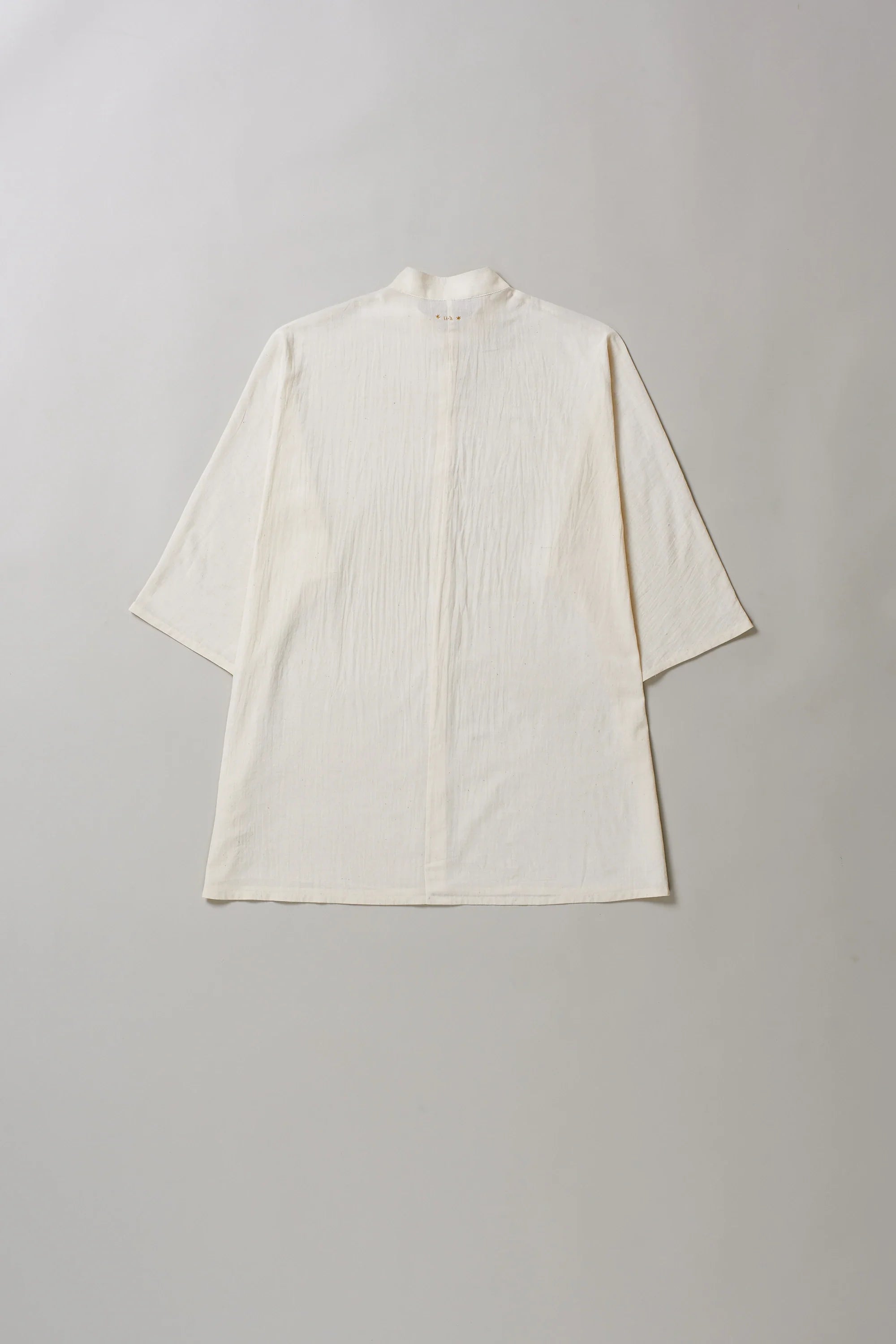 Back image of ecru cotton shirt with buttons on a grey background