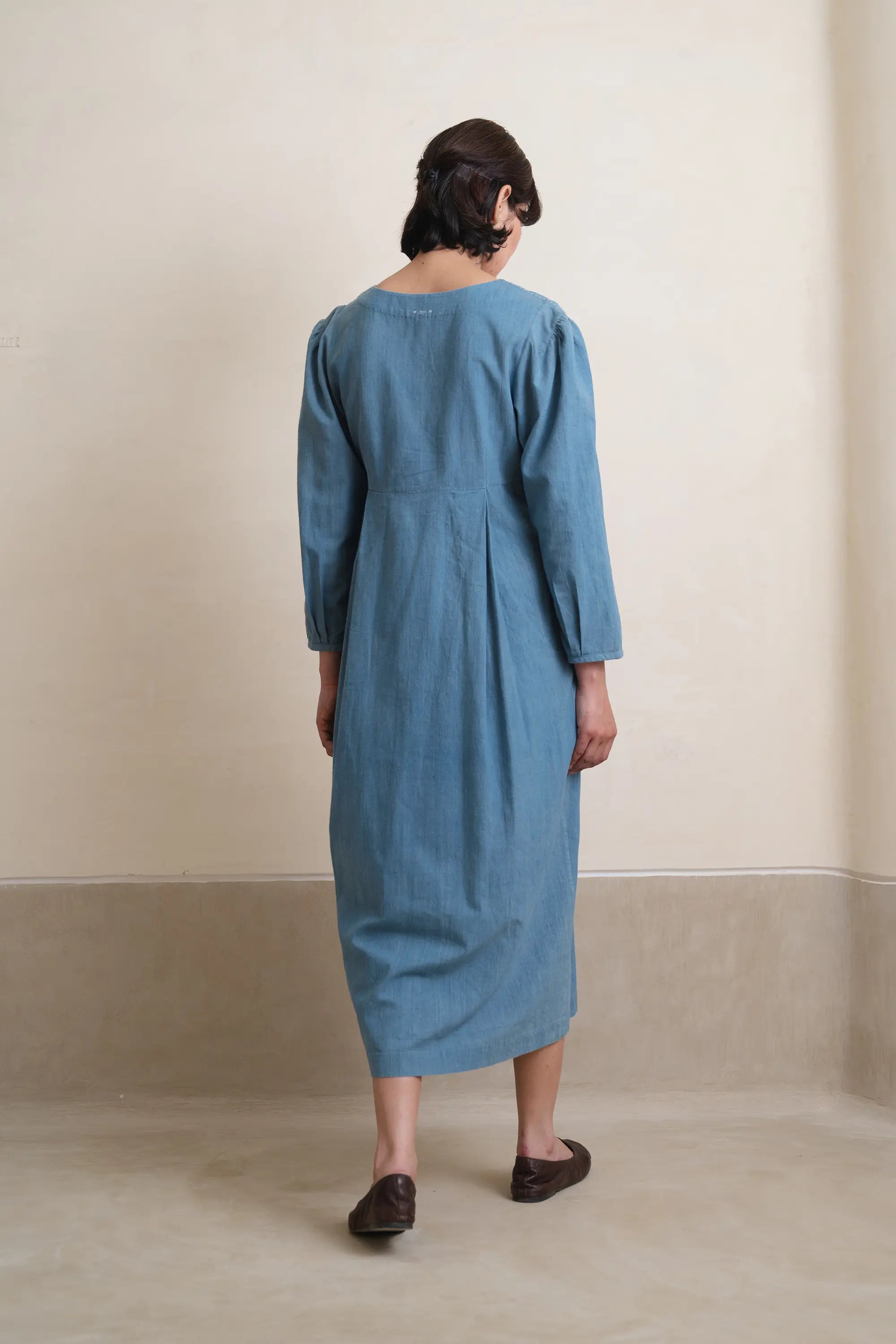 A woman wearing a blue dress standing against a plain background