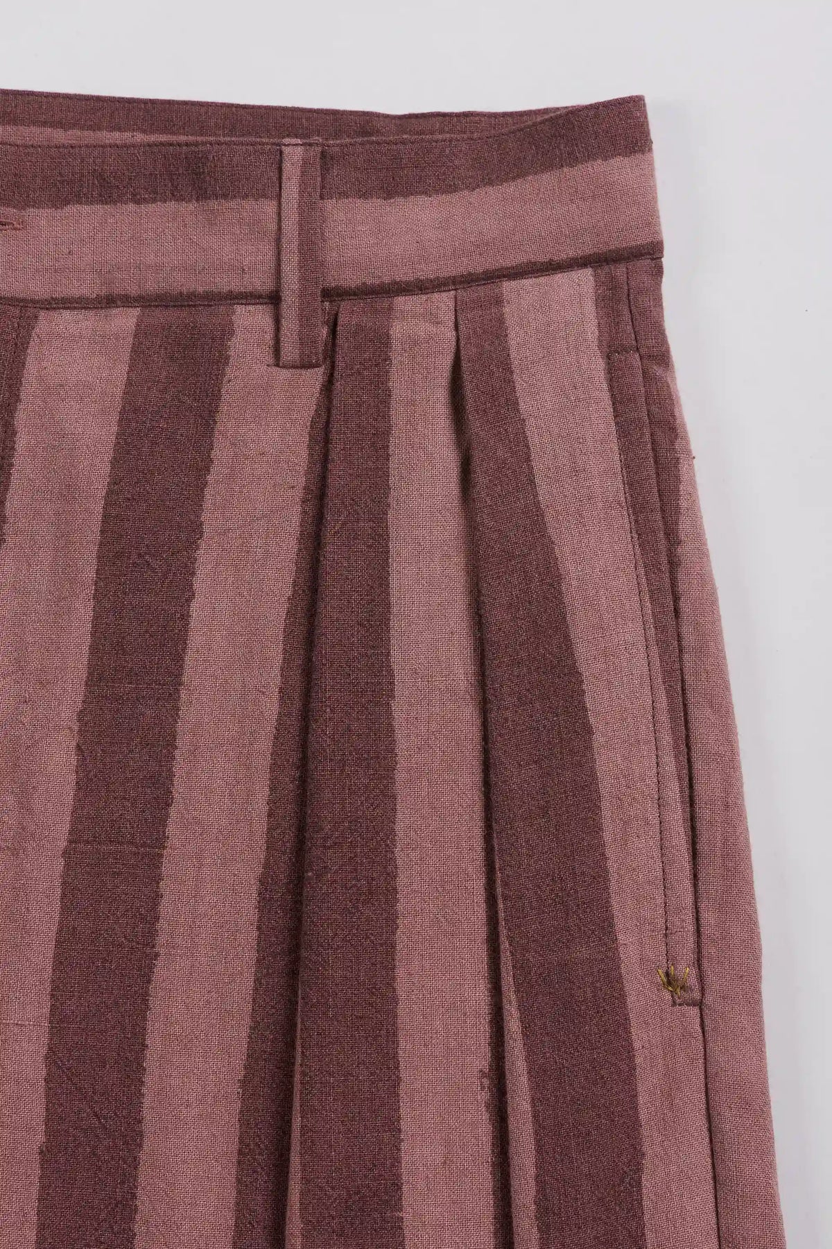 Close-up of pleated trousers featuring vertical stripes in dusty rose and dark brown, with a matching waistband.