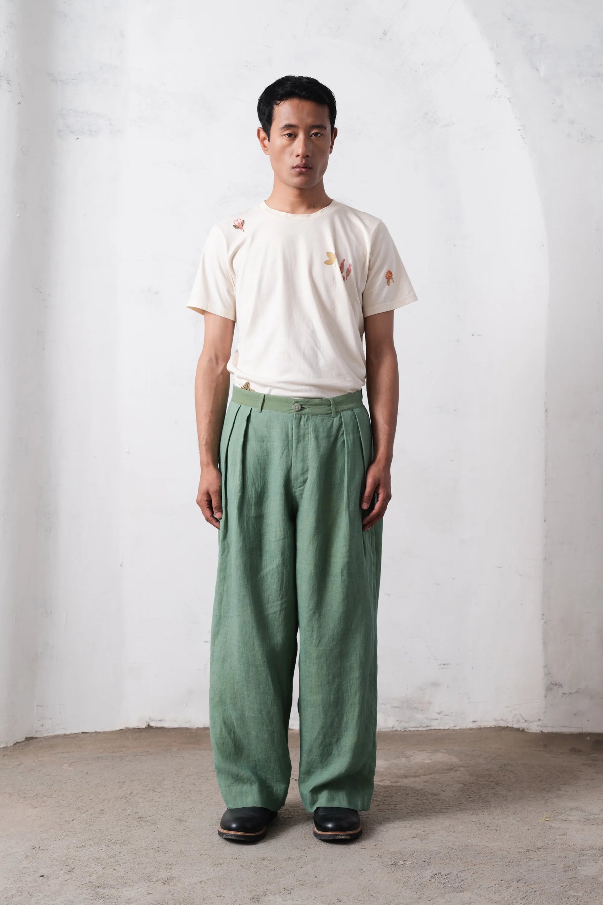 Person wearing a white t-shirt and green pants against a light grey wall