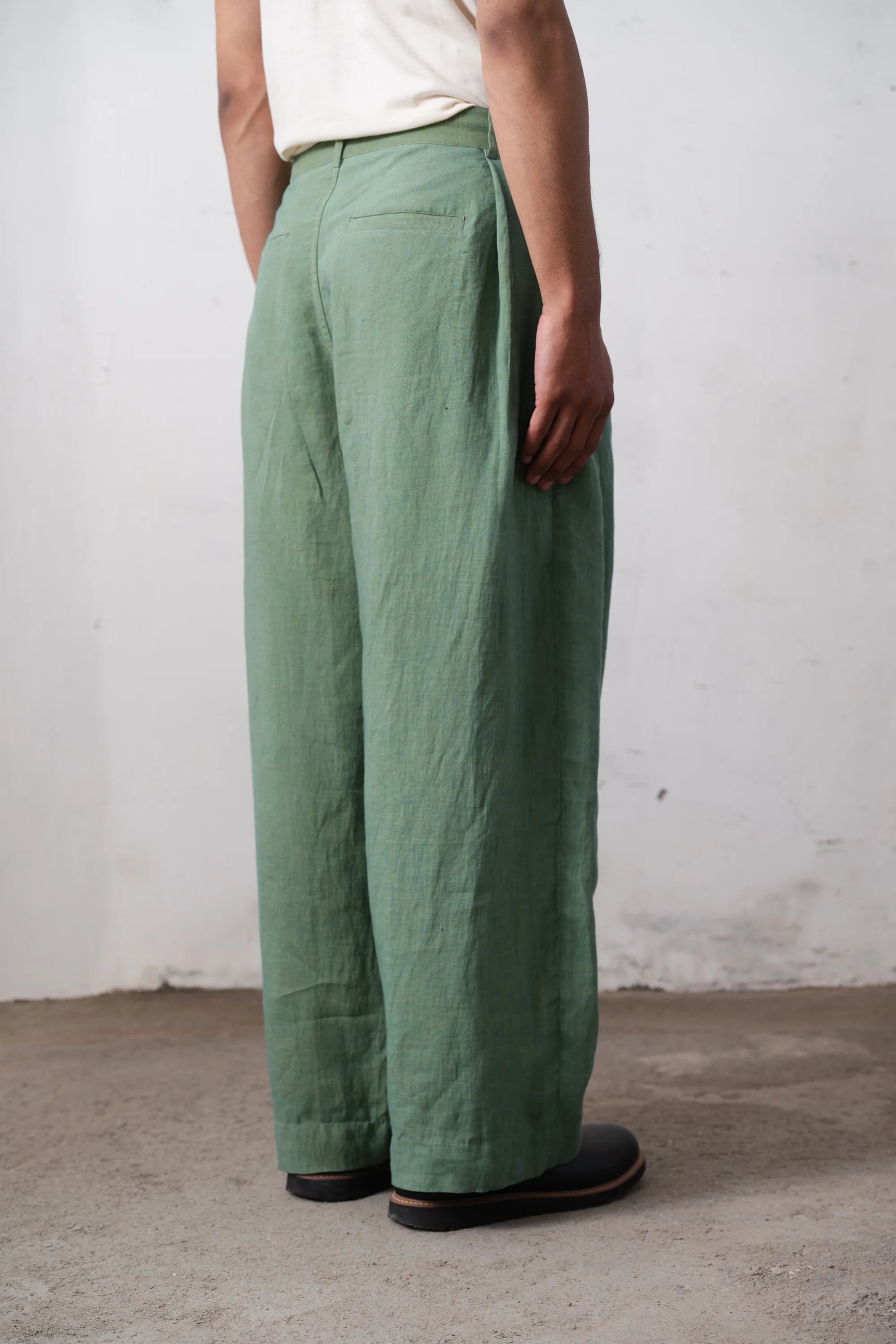 A side shot of a person wearing green pants against a light grey wall