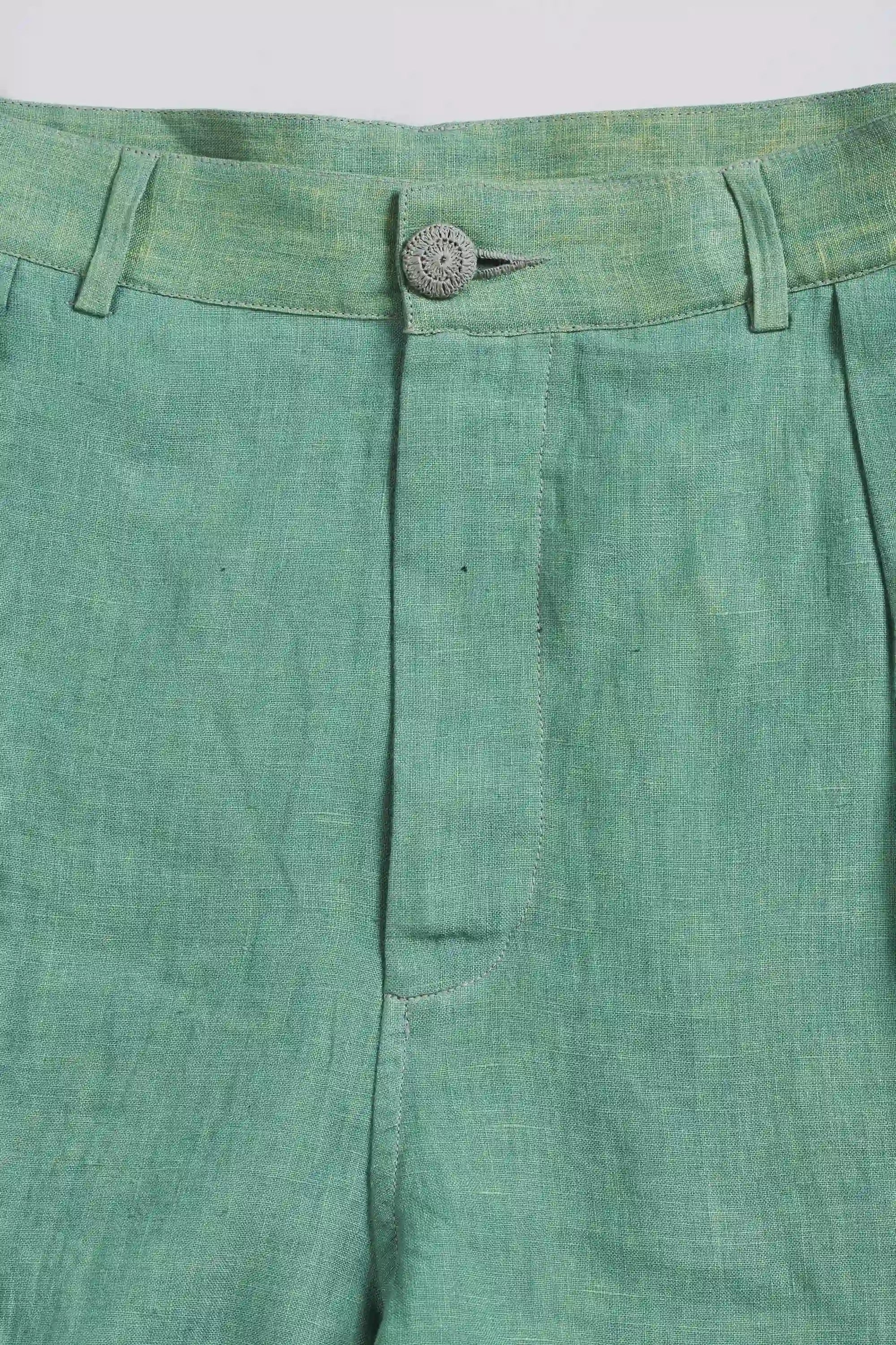 Close-up of green pleated pants with a button on a light grey background