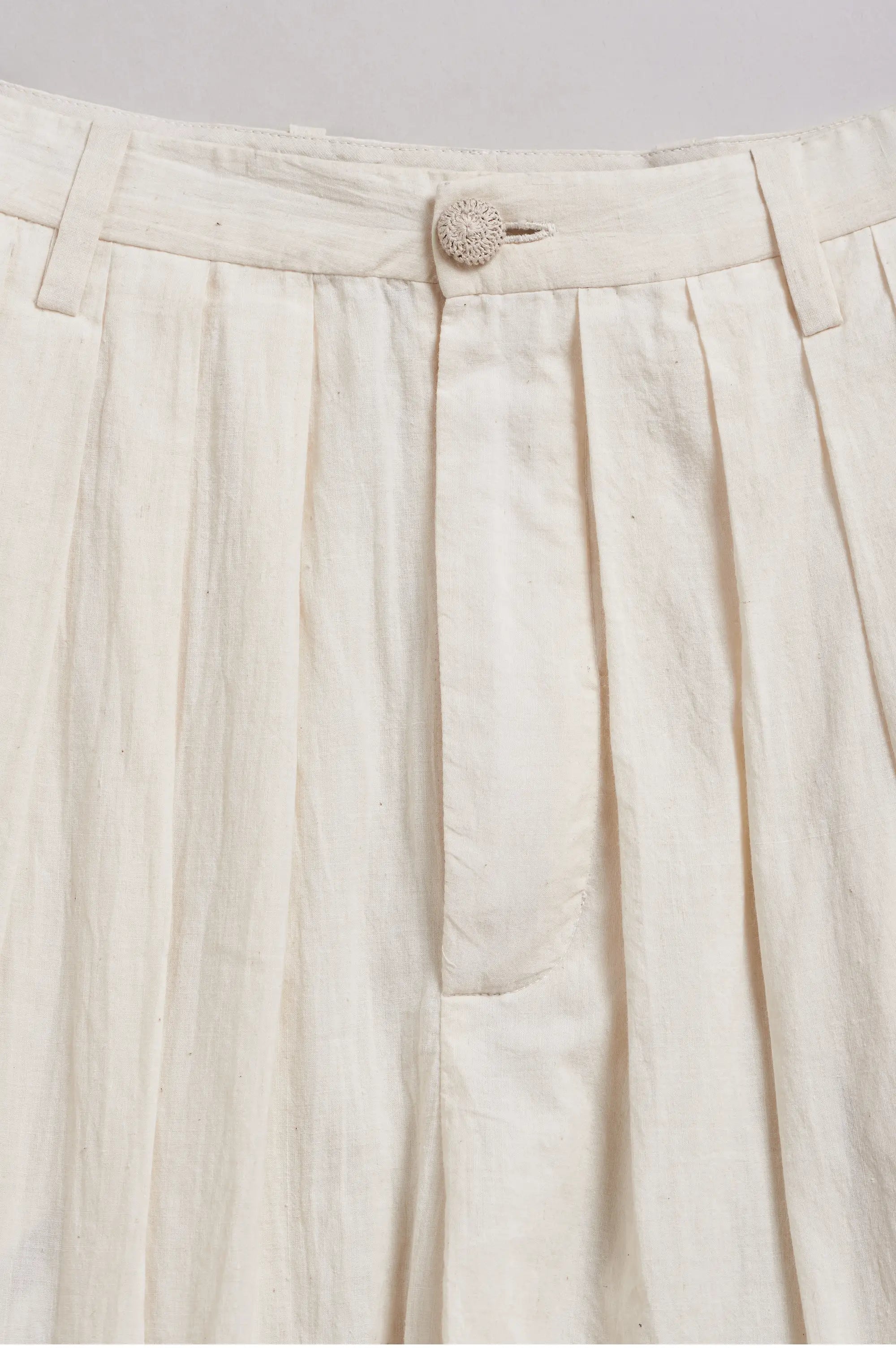 Close-up of a ecru pleated pant with a button on a light grey background