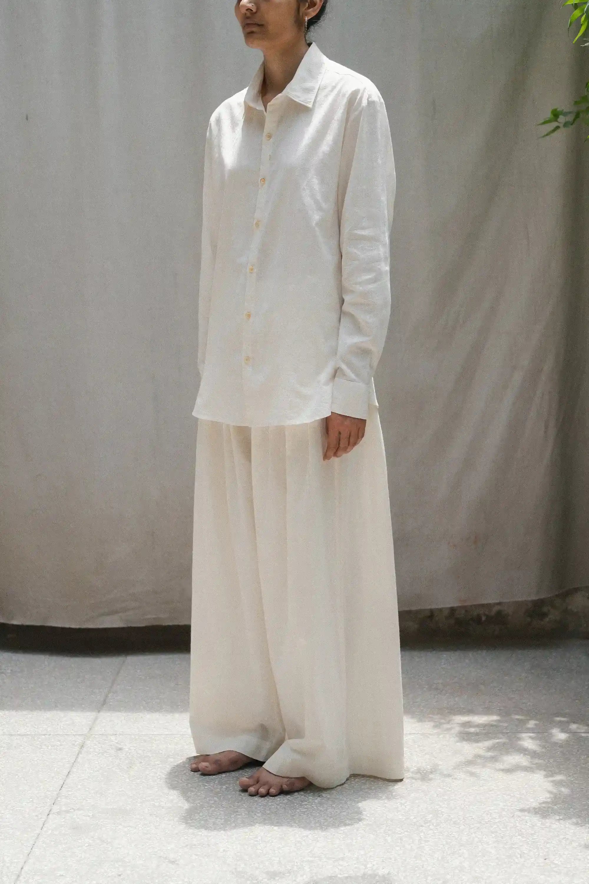 Person wearing a ecru shirt and ecru pants against a plain background