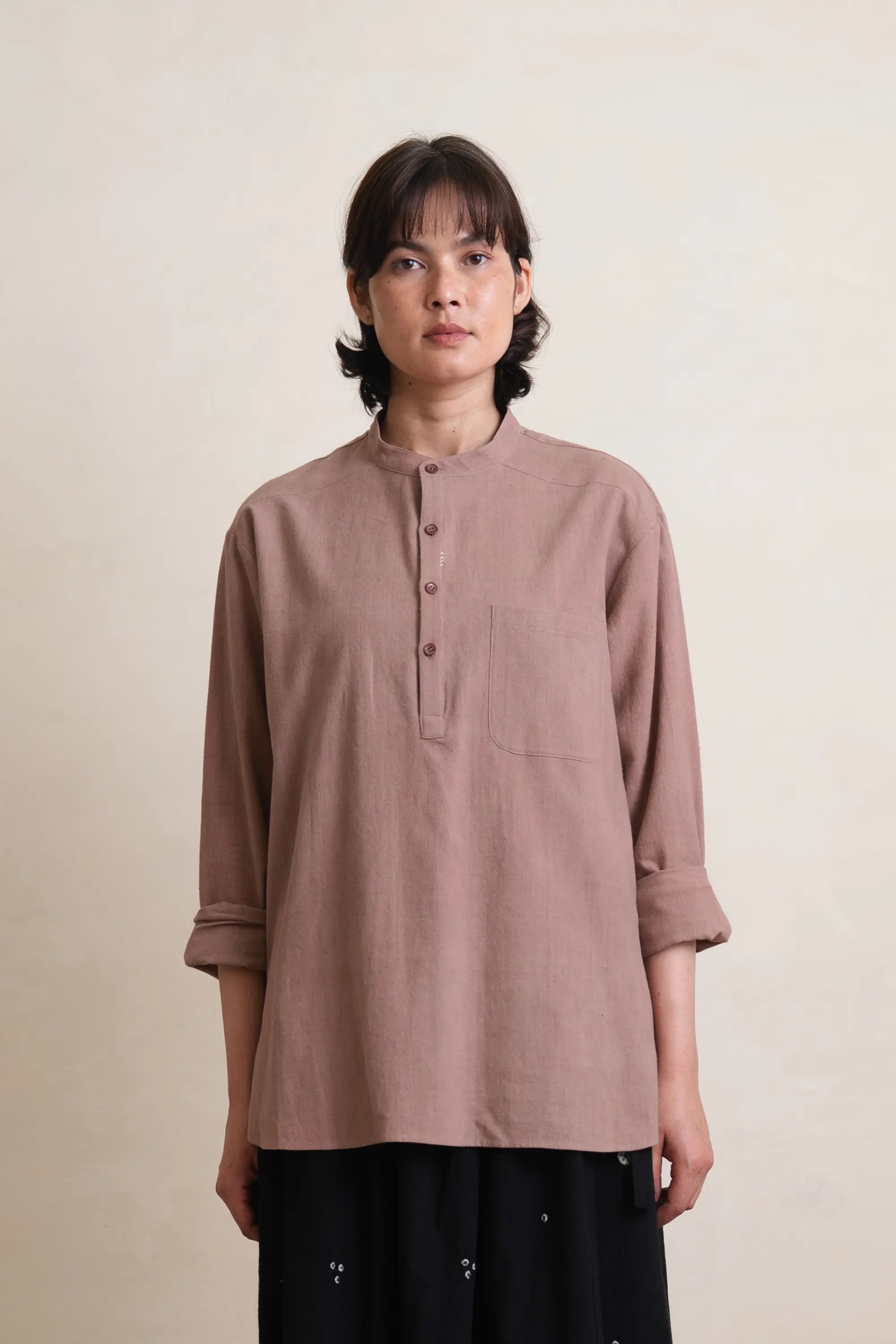 Person wearing a brown long-sleeve shirt with a pocket on a beige background