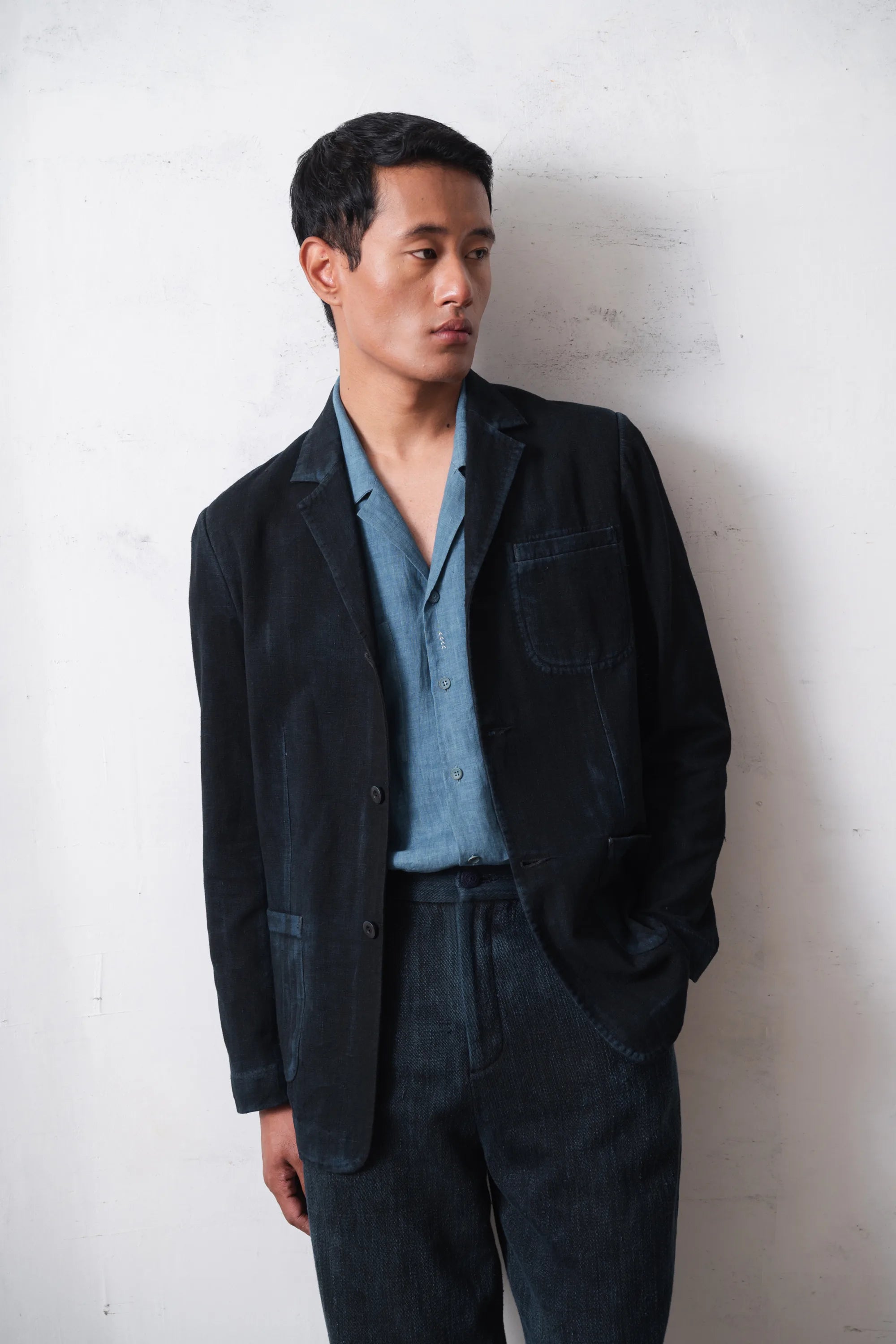 Man wearing a black jacket and light blue shirt against a light grey background