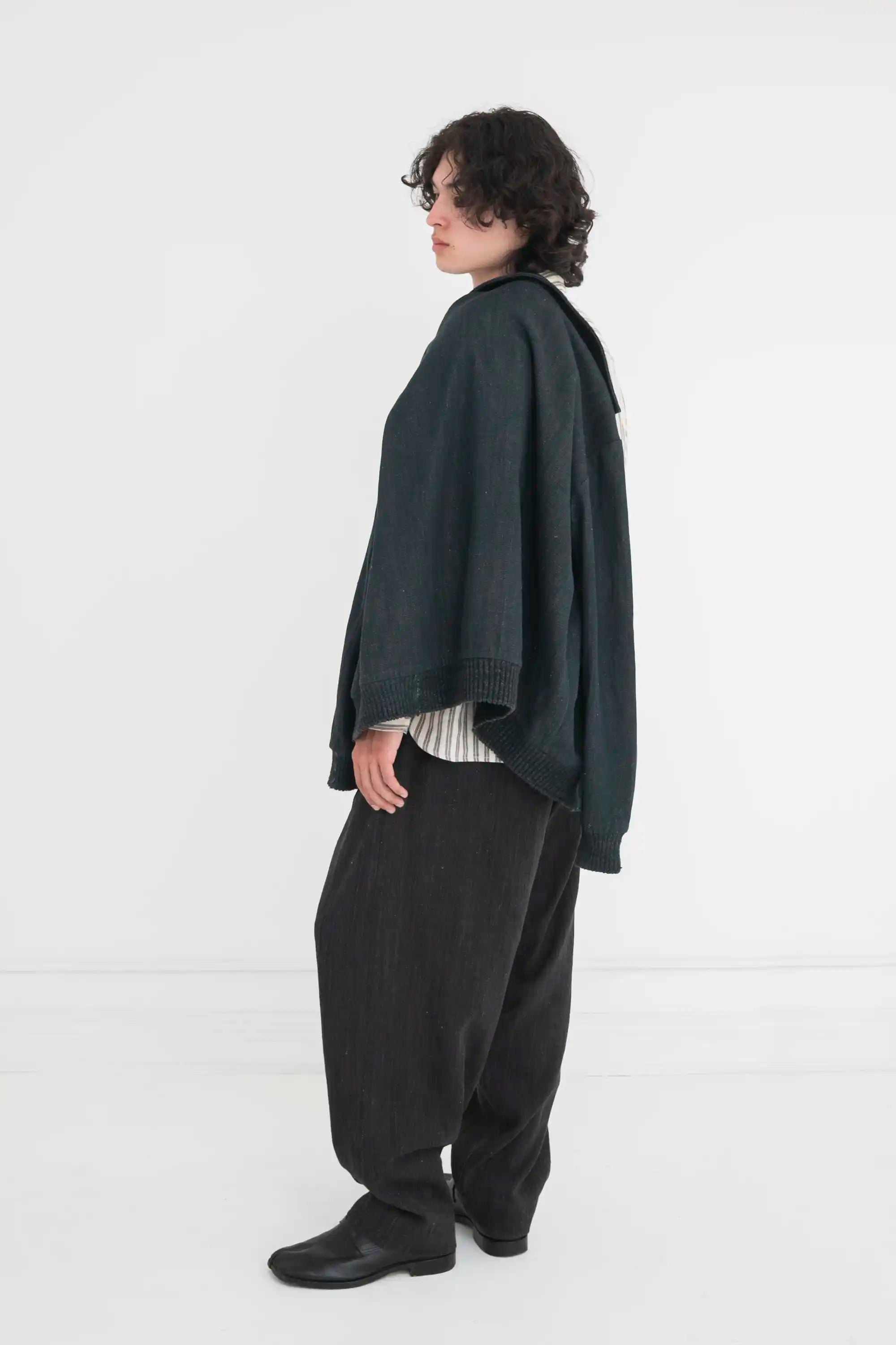 Man wearing a midnight indigo jacket over a striped shirt and pants on a grey background