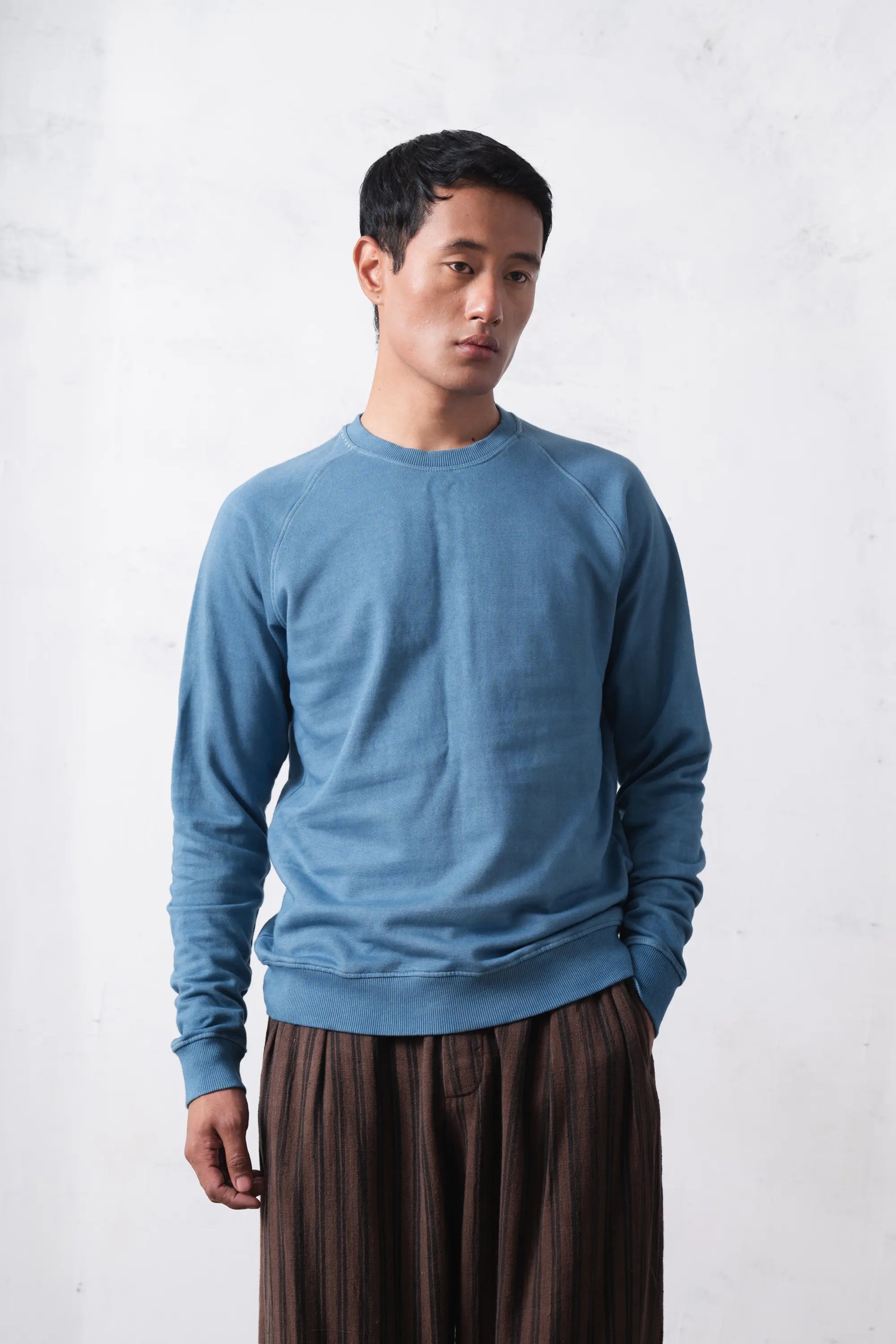Man wearing a blue sweater and brown pants against a white background