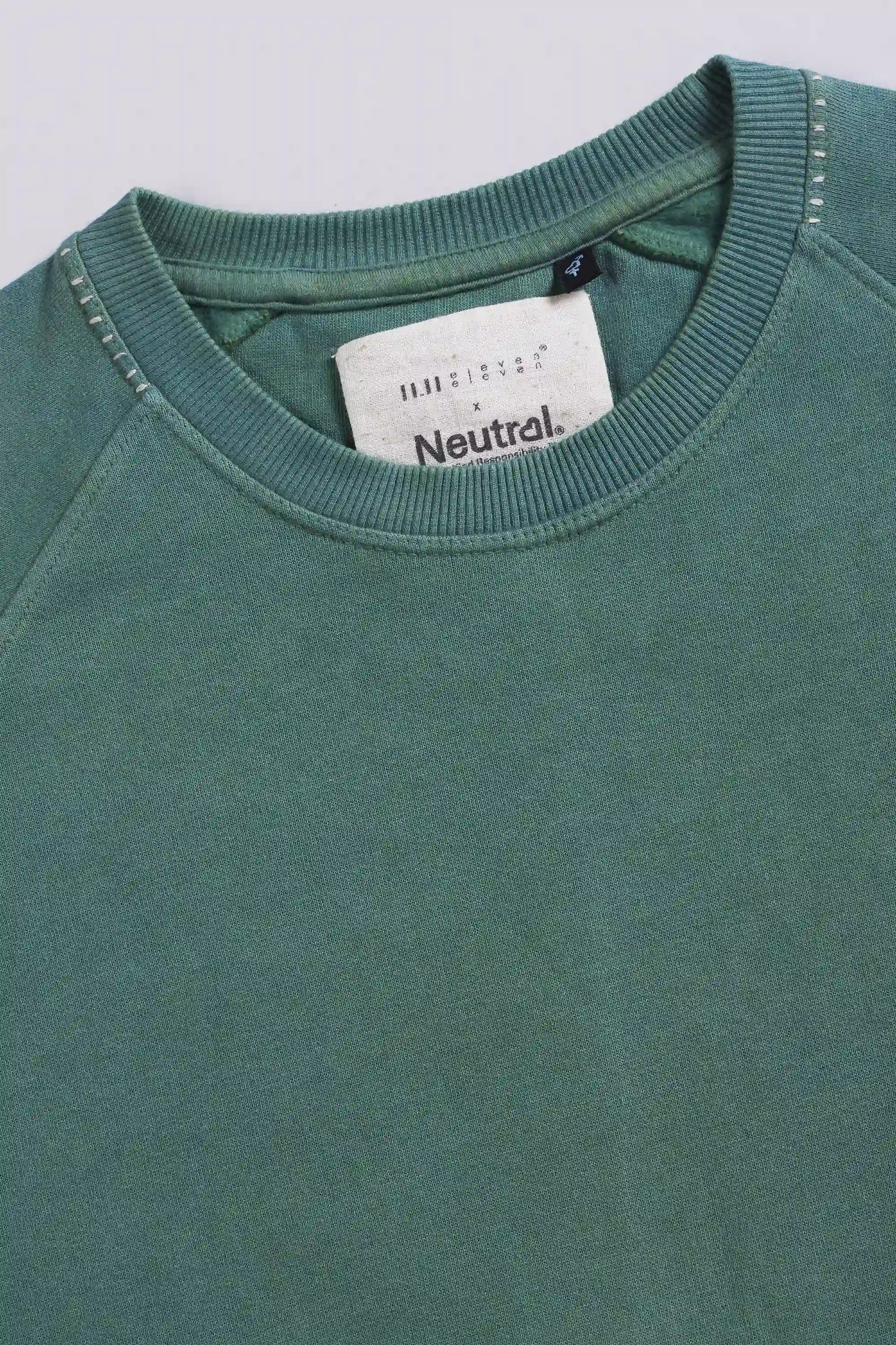 Close-up of a green sweatshirt with a brand label on a light grey background