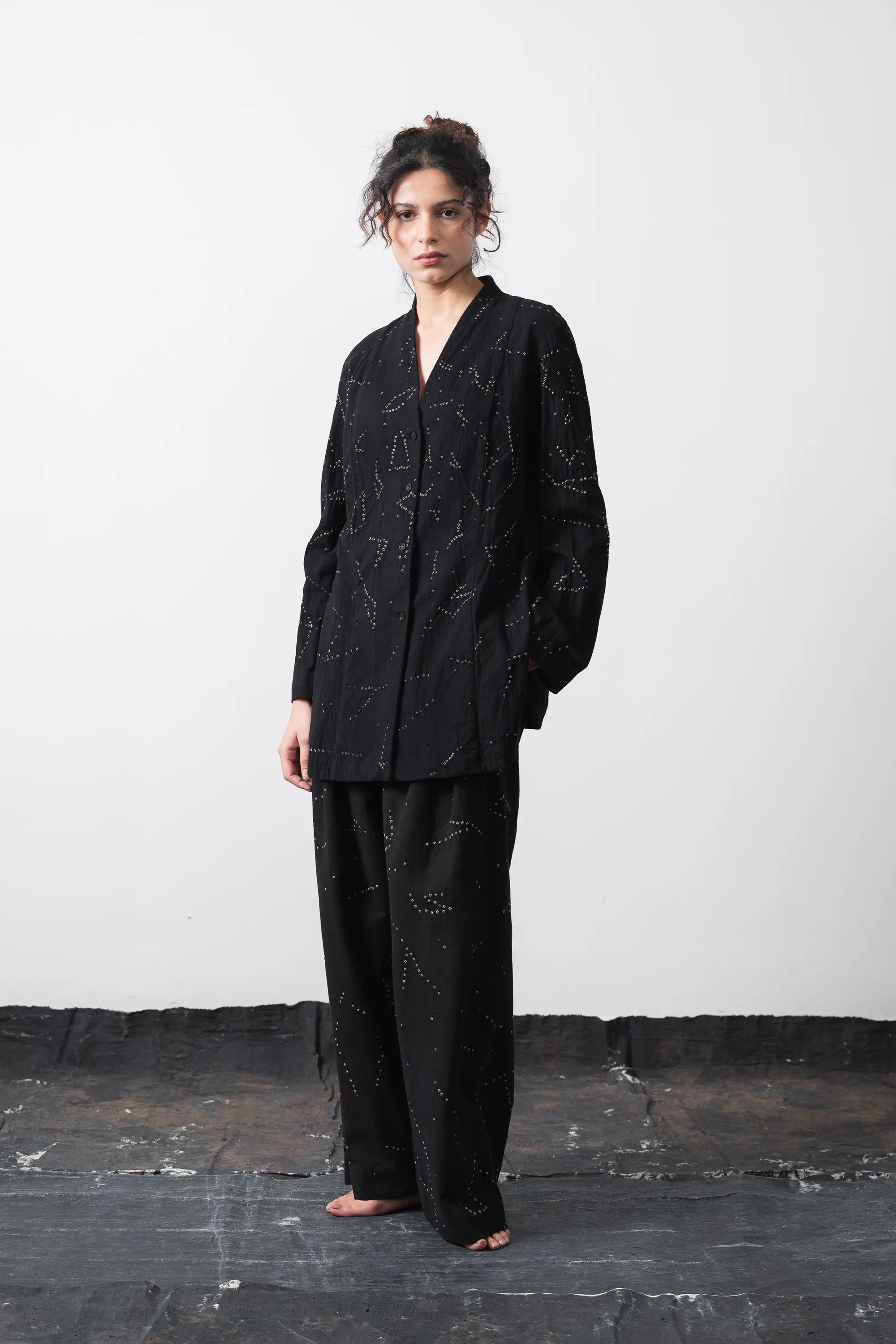A model wearing a black long-sleeve kimono-style shirt with white dotted star patterns, paired with matching black pants, against a plain light grey background.