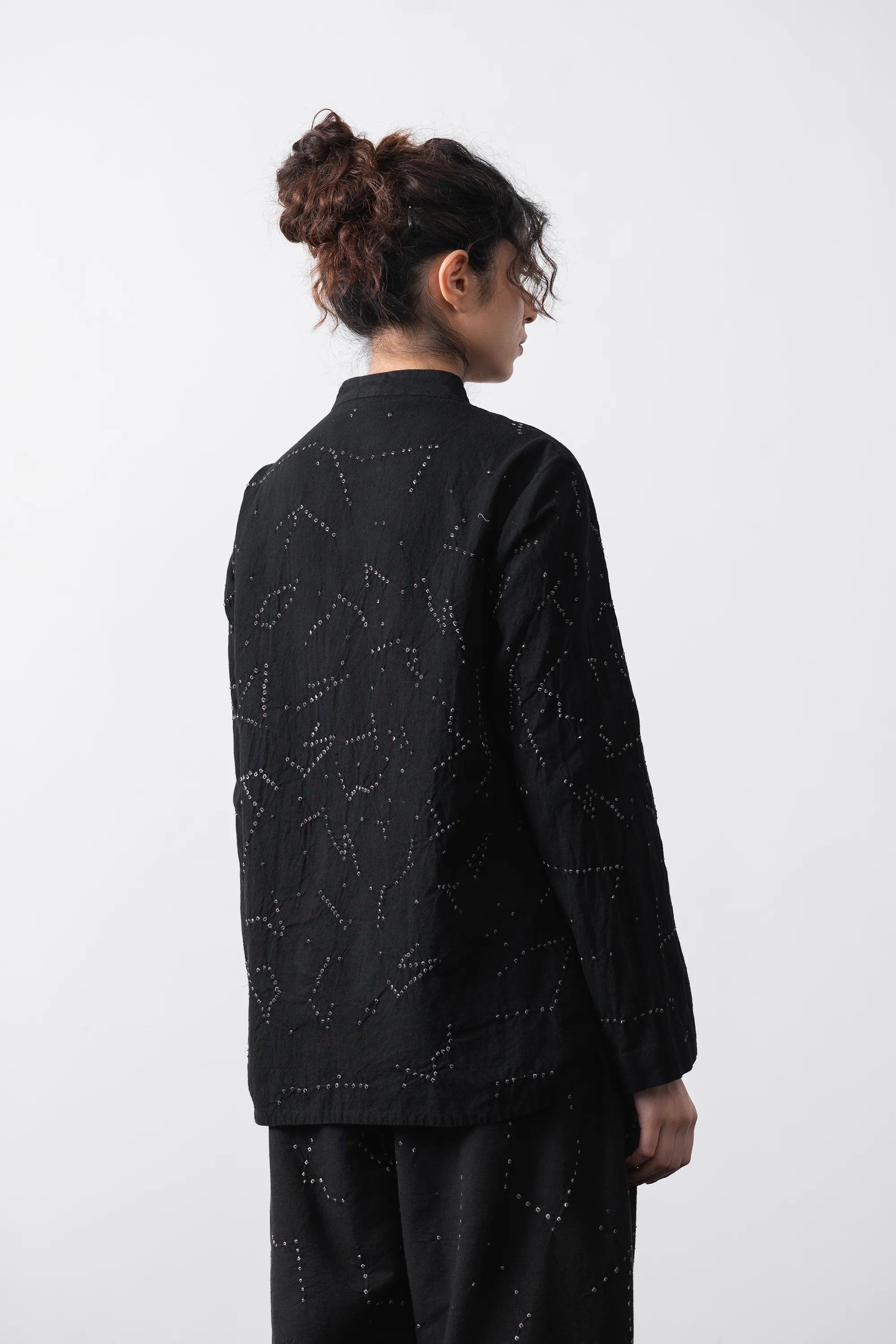 A model shown from the back wearing a black long-sleeve shirt and matching pants, with shibori artwork, against a plain white studio background.