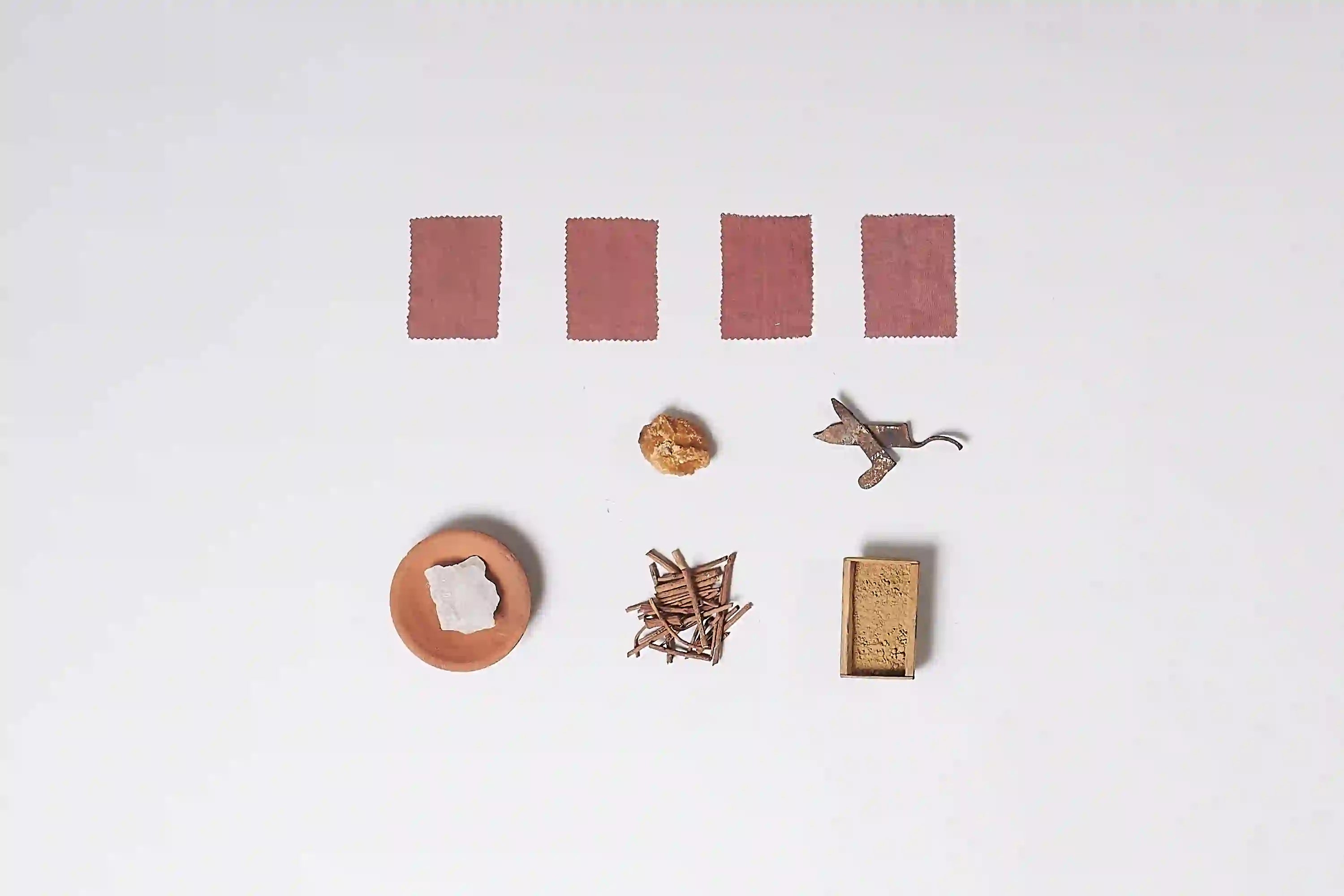 Set of miniature items including fabric swatches, a small round object, a piece of iron, and other small objects on a white background.