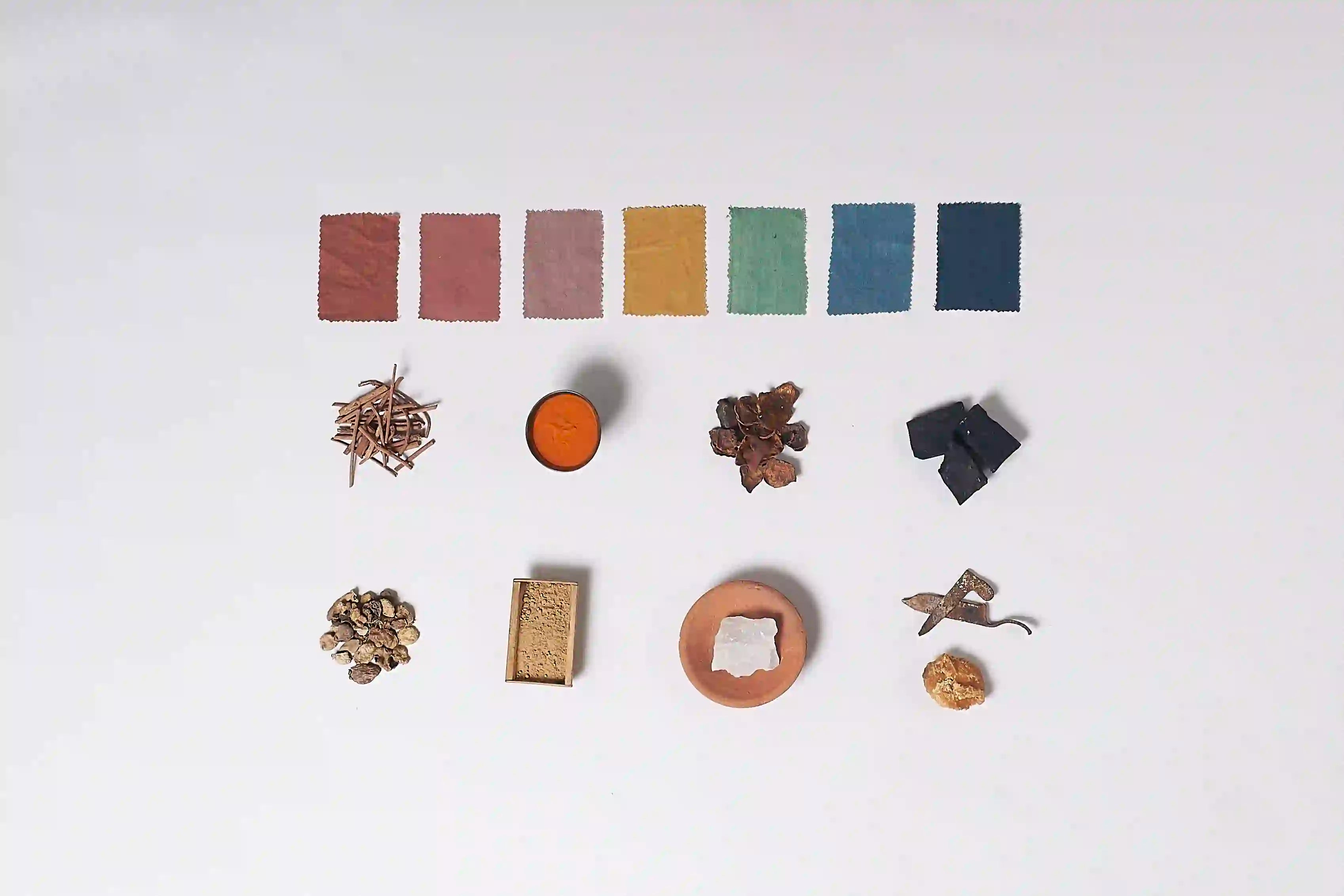 Set of miniature items including fabric swatches, a small round object, a piece of iron, and other small objects on a white background.