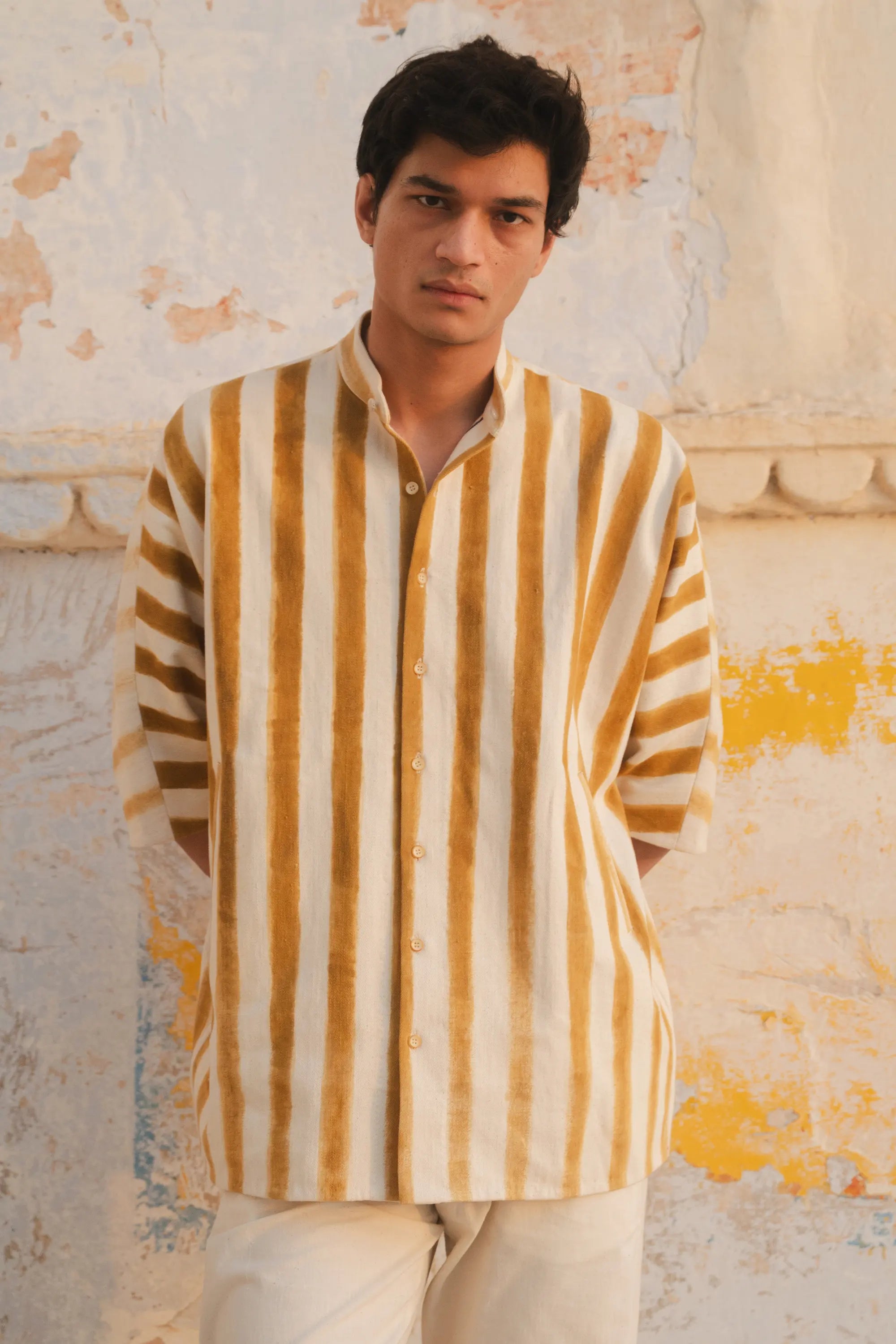 Close-up shot of a man wearing a yellow and white striped shirt against a textured wall.