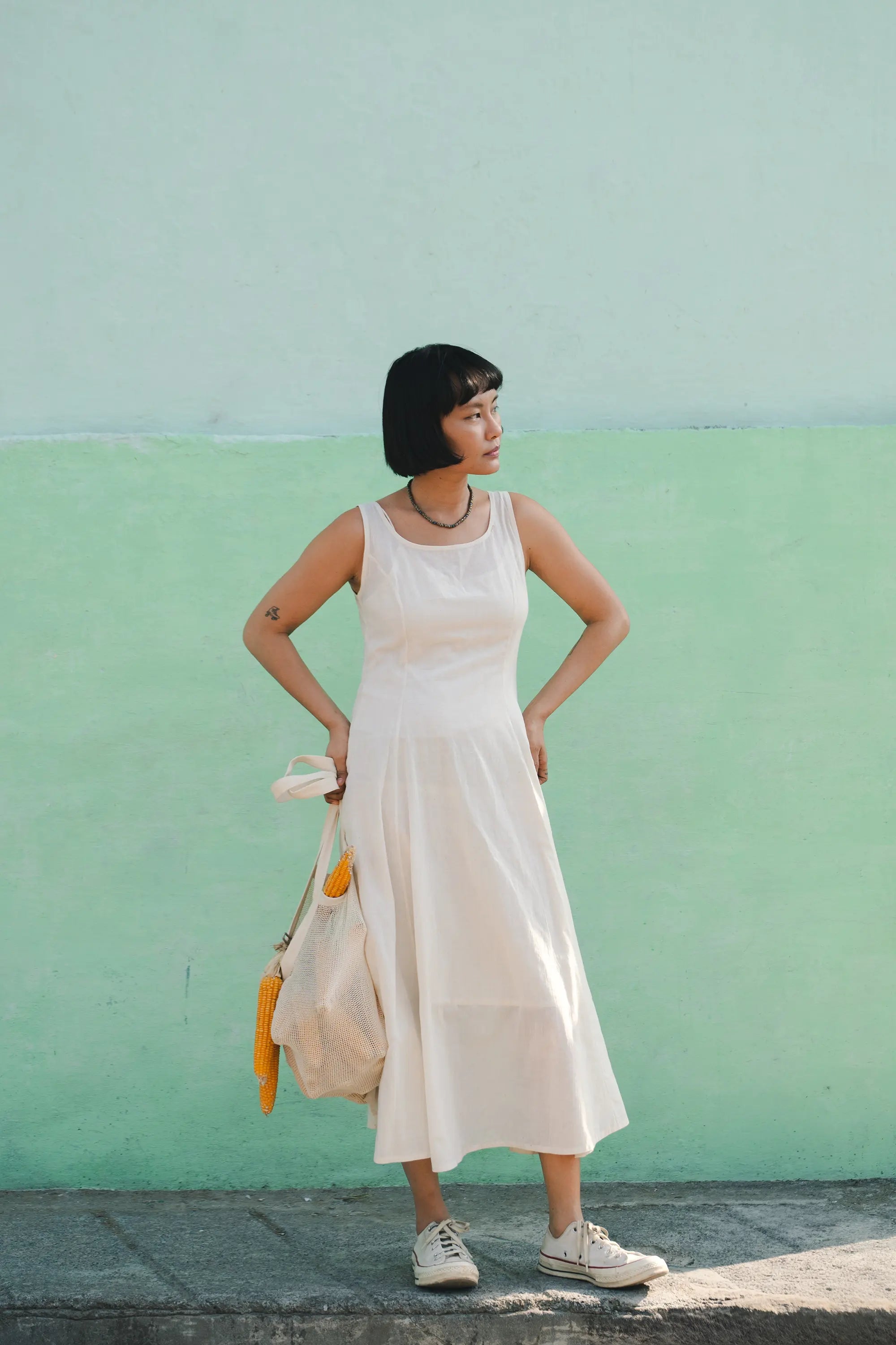 Woman in a white dress standing against a green wall
