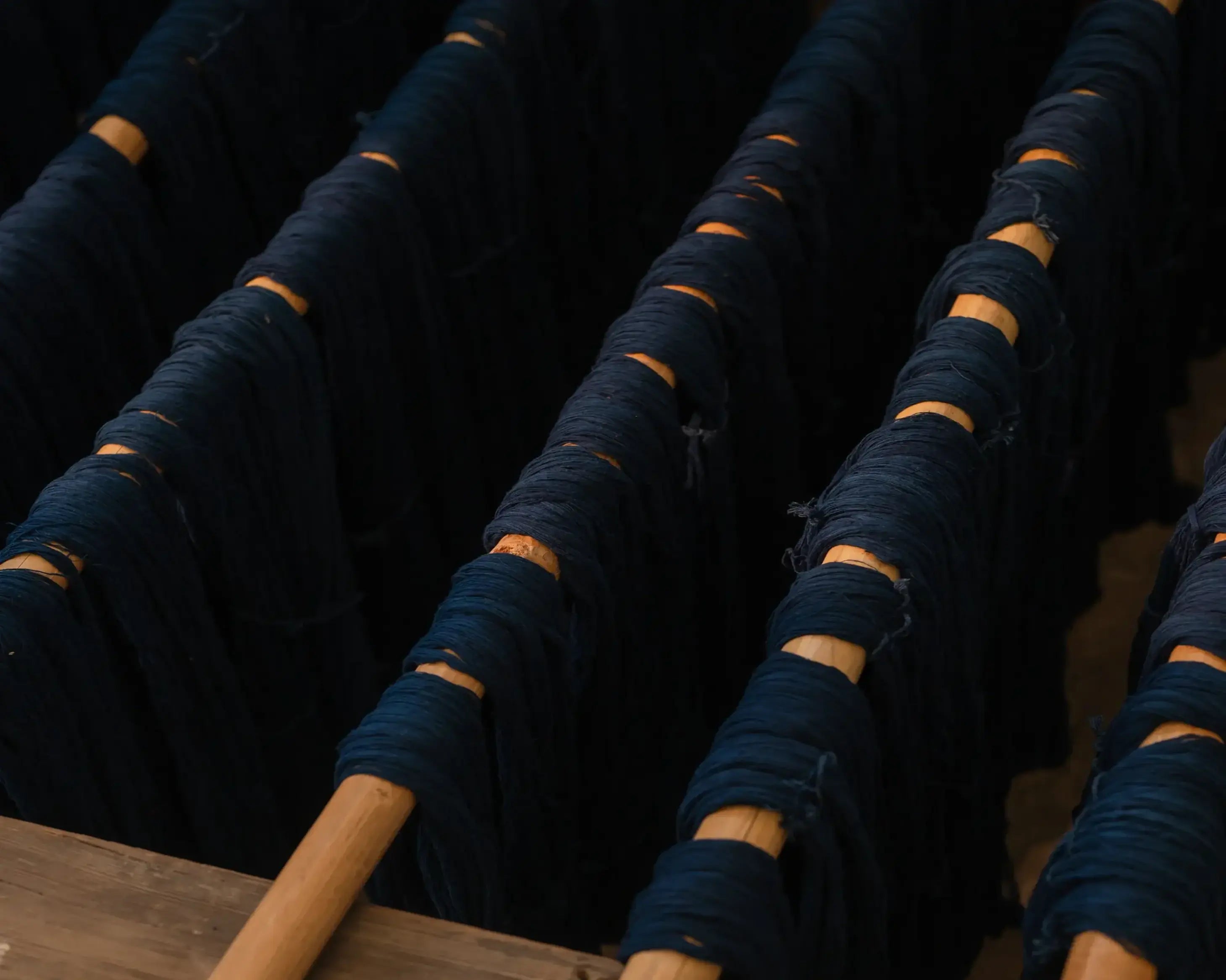Indigo yarn rolls stacked on a wooden rack against a dark background