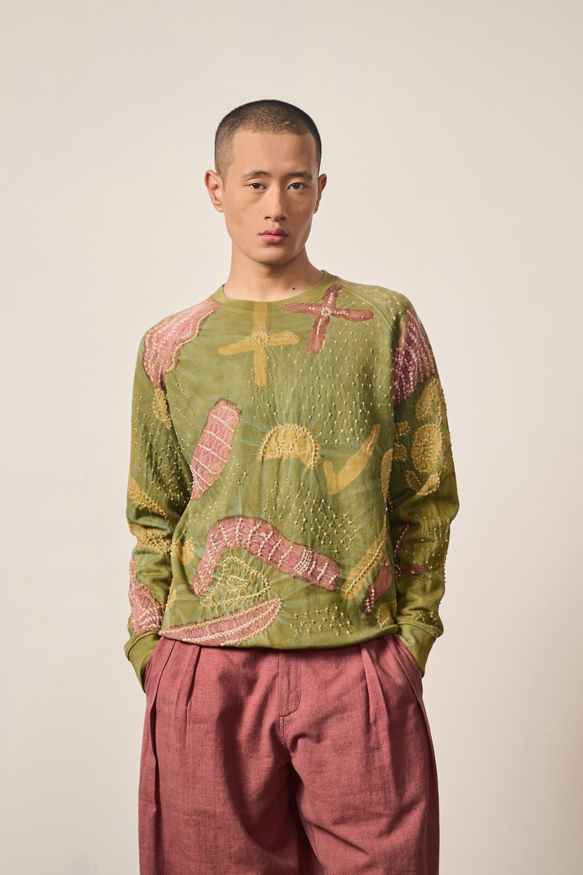 Man wearing a moss green patterned sweatshirt on a grey background