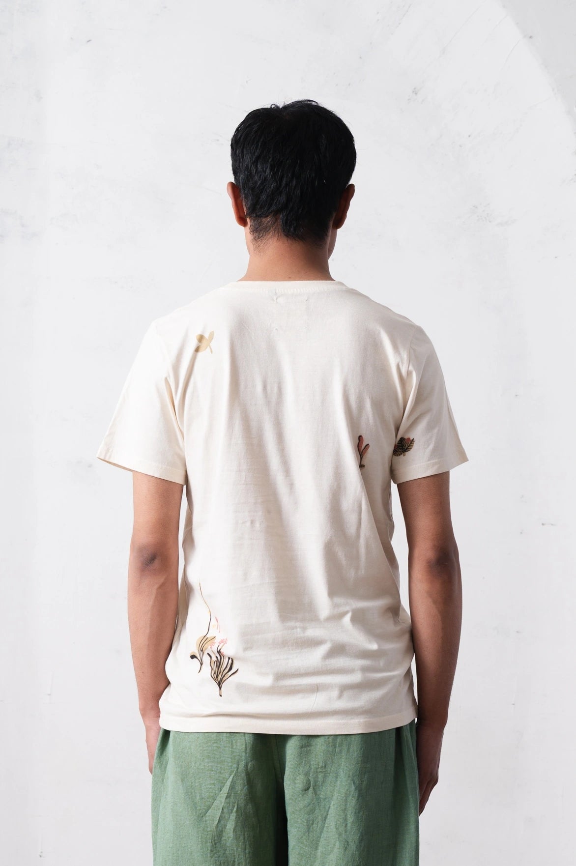 Back shot of a person wearing a white t-shirt with floral designs on a light grey background