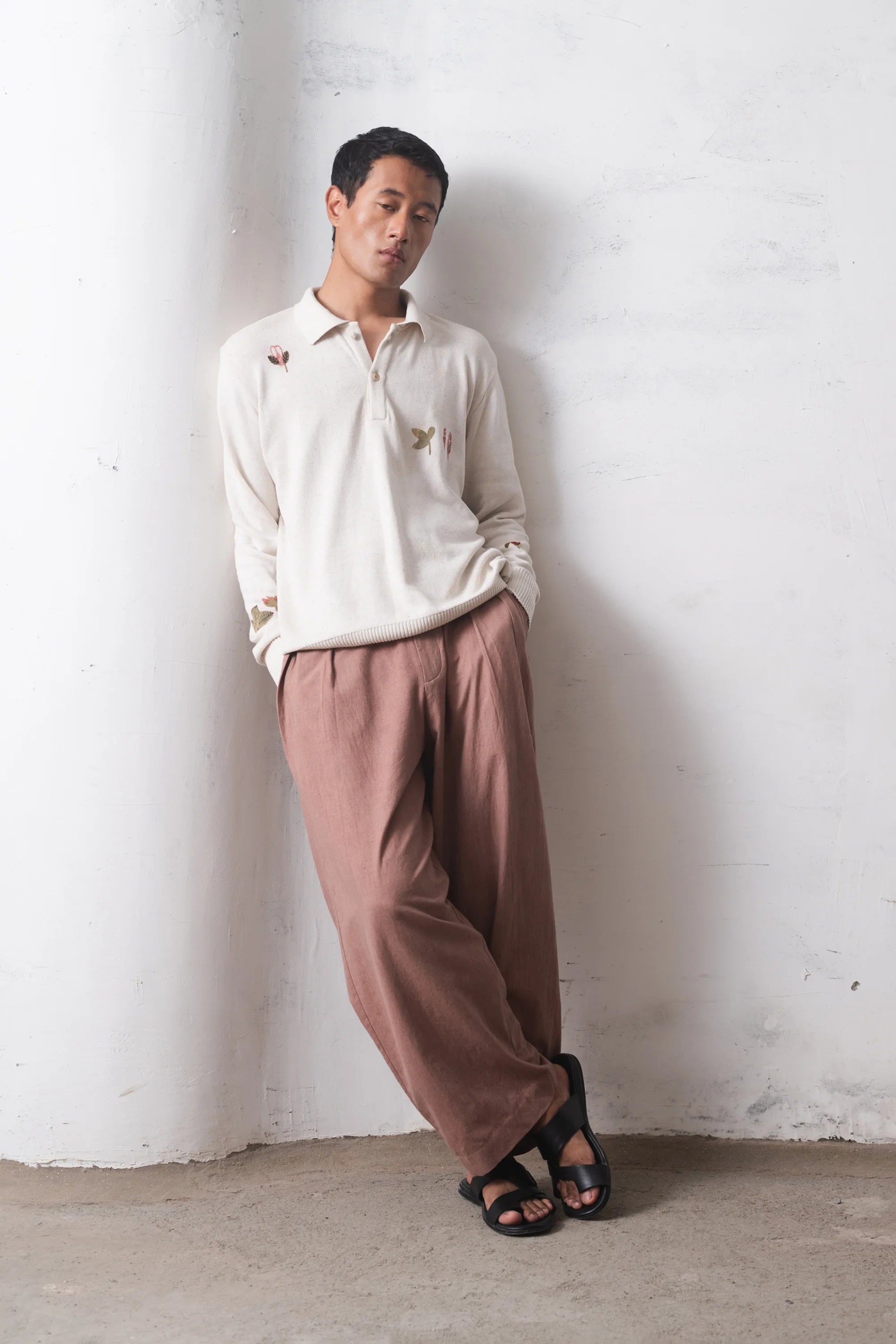 Person wearing a light-colored t-shirt and brown pants against a white wall