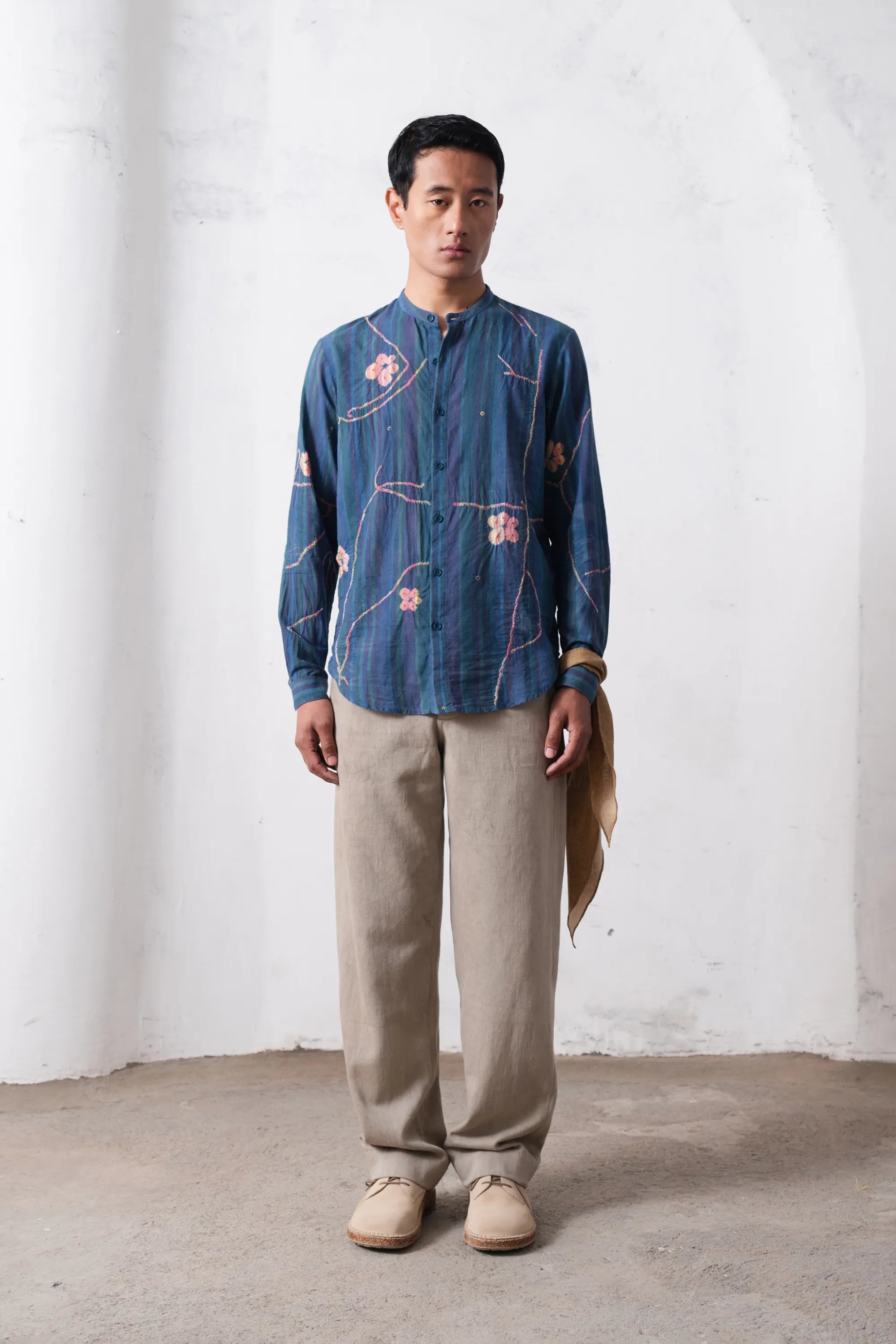 Man wearing a blue shirt and beige pants against a white wall