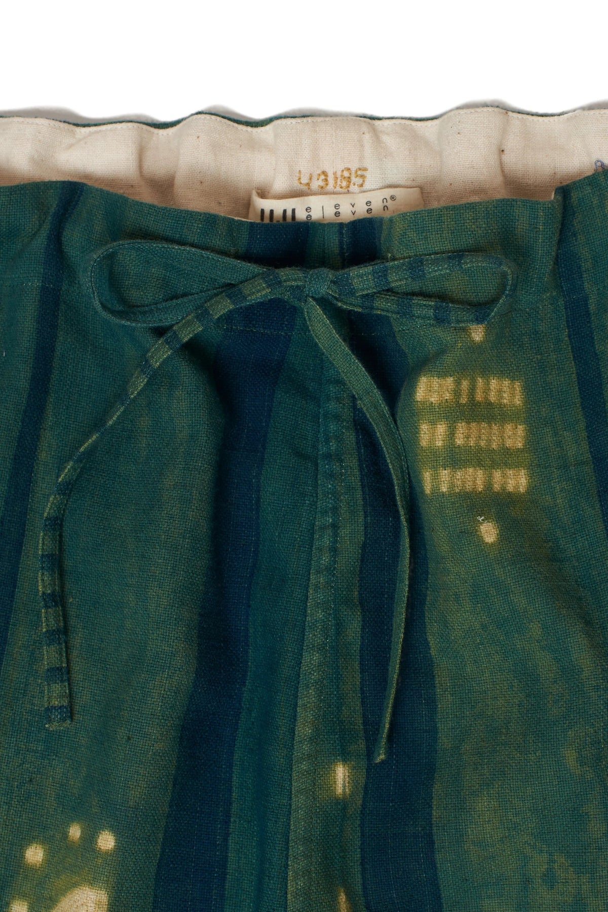 Close-up of Bottle green pants with a button and label on a grey background