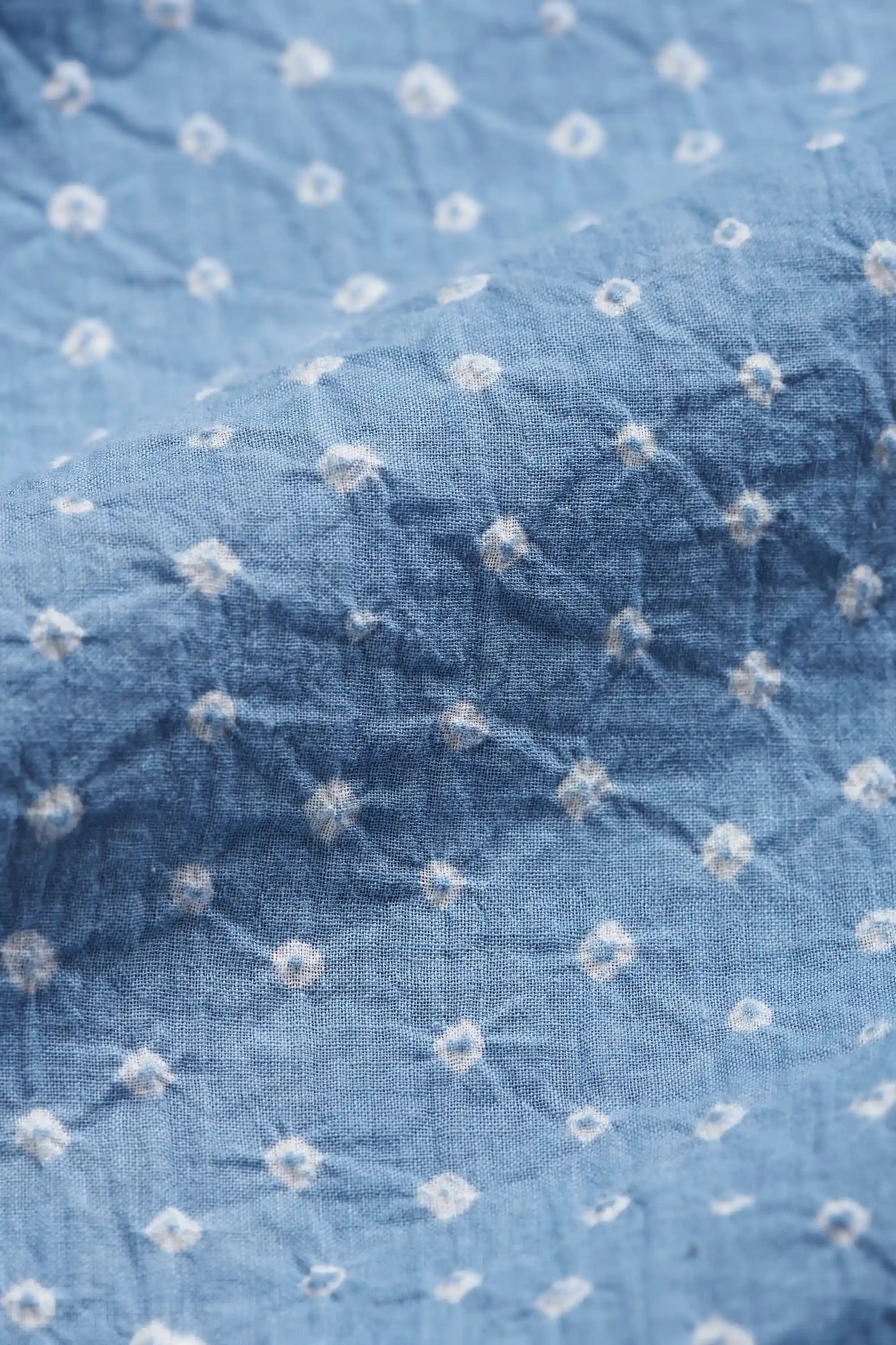 Close-up of light indigo fabric with a white shibori tie-dye pattern.