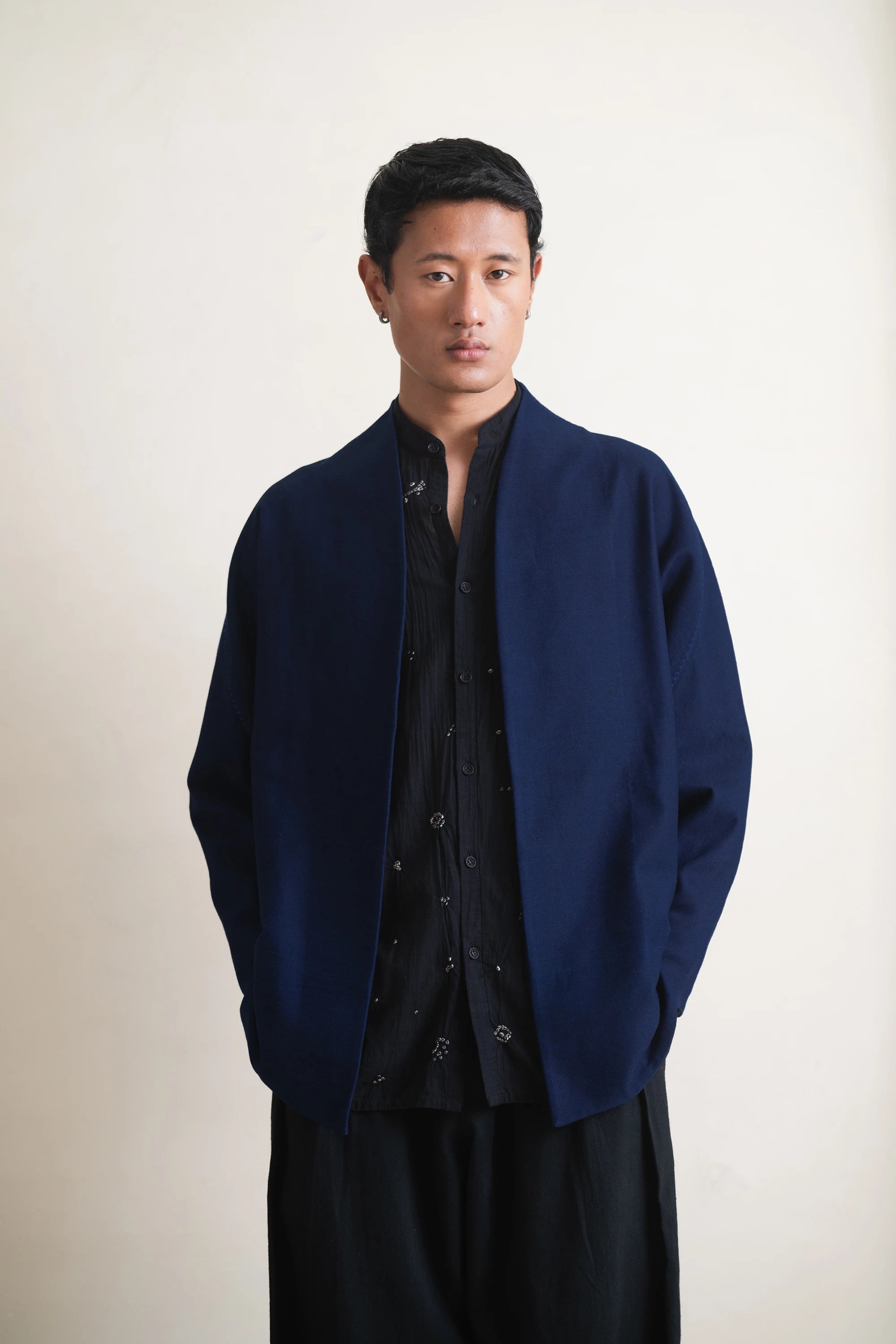 Man wearing a indigo coat over a black shirt against a light grey background
