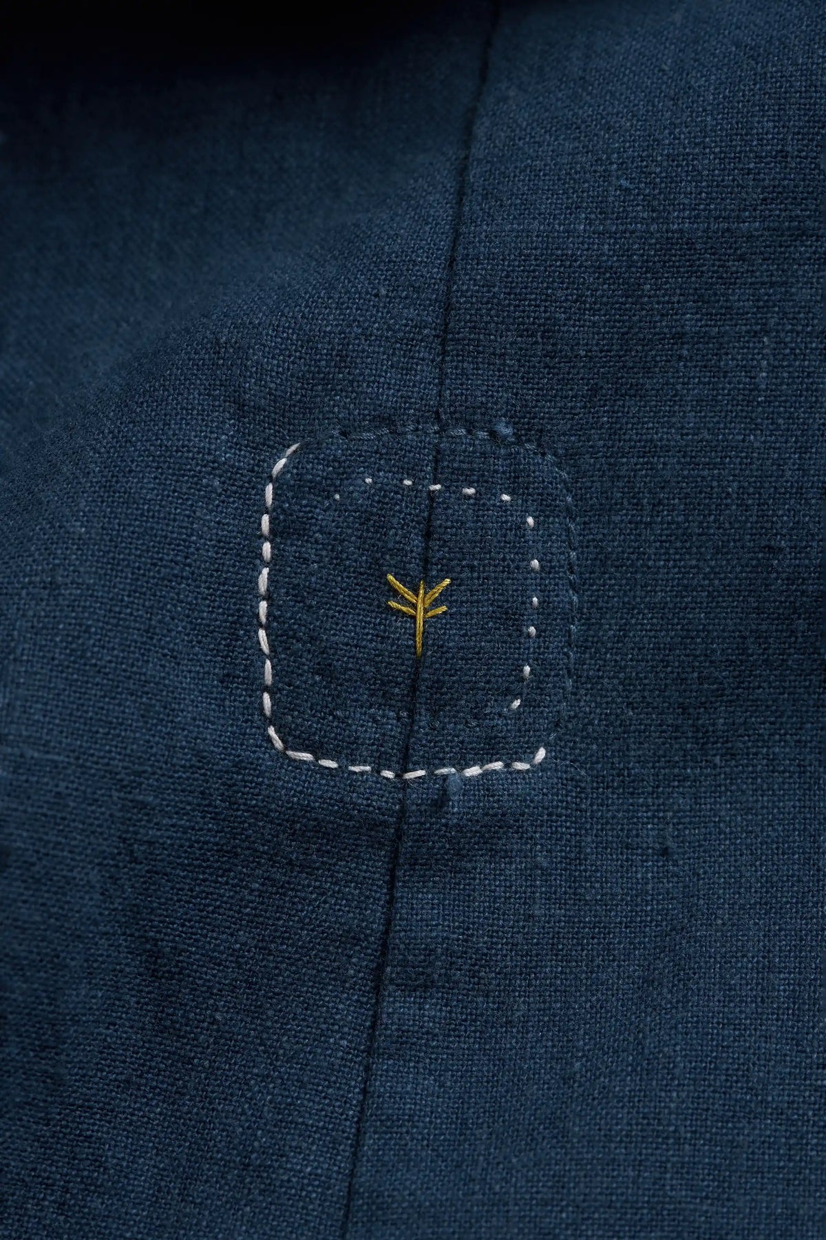 Close-up of dark navy blue fabric with small yellow embroidered symbol.