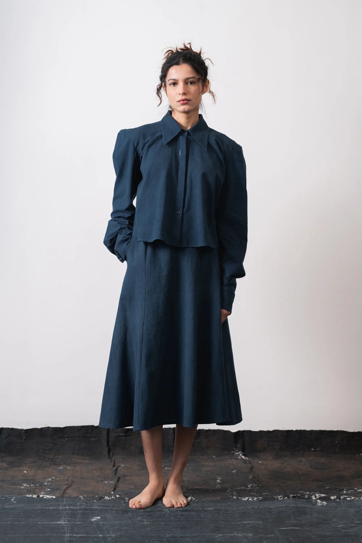 A black indigo cropped long-sleeve button-up shirt with a pointed collar, laid flat against a light grey background.