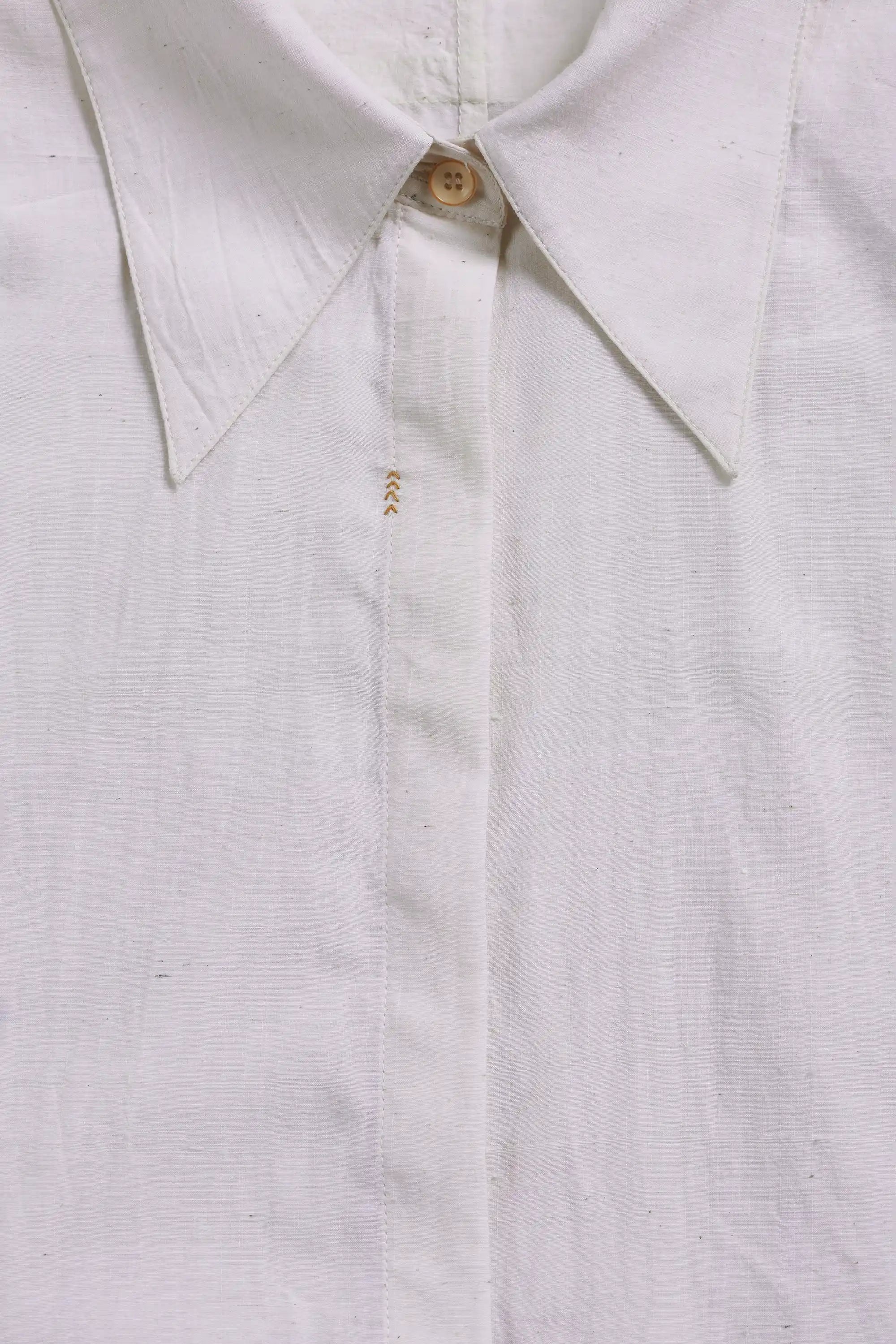 Close-up of a white linen button-down shirt collar with a single wooden button and subtle gold embroidery.