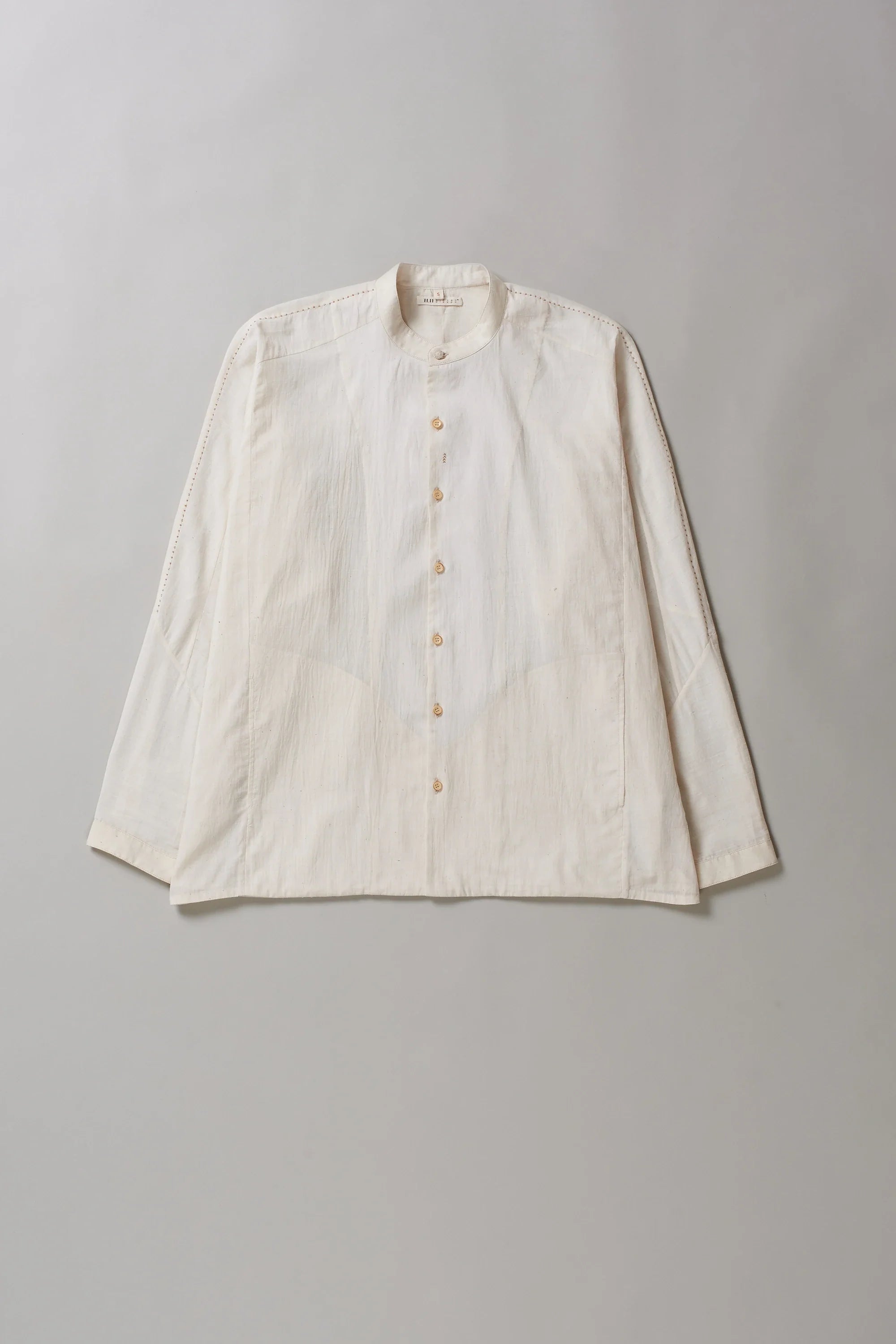 Front image of ecru cotton shirt with hand detailing on a grey background