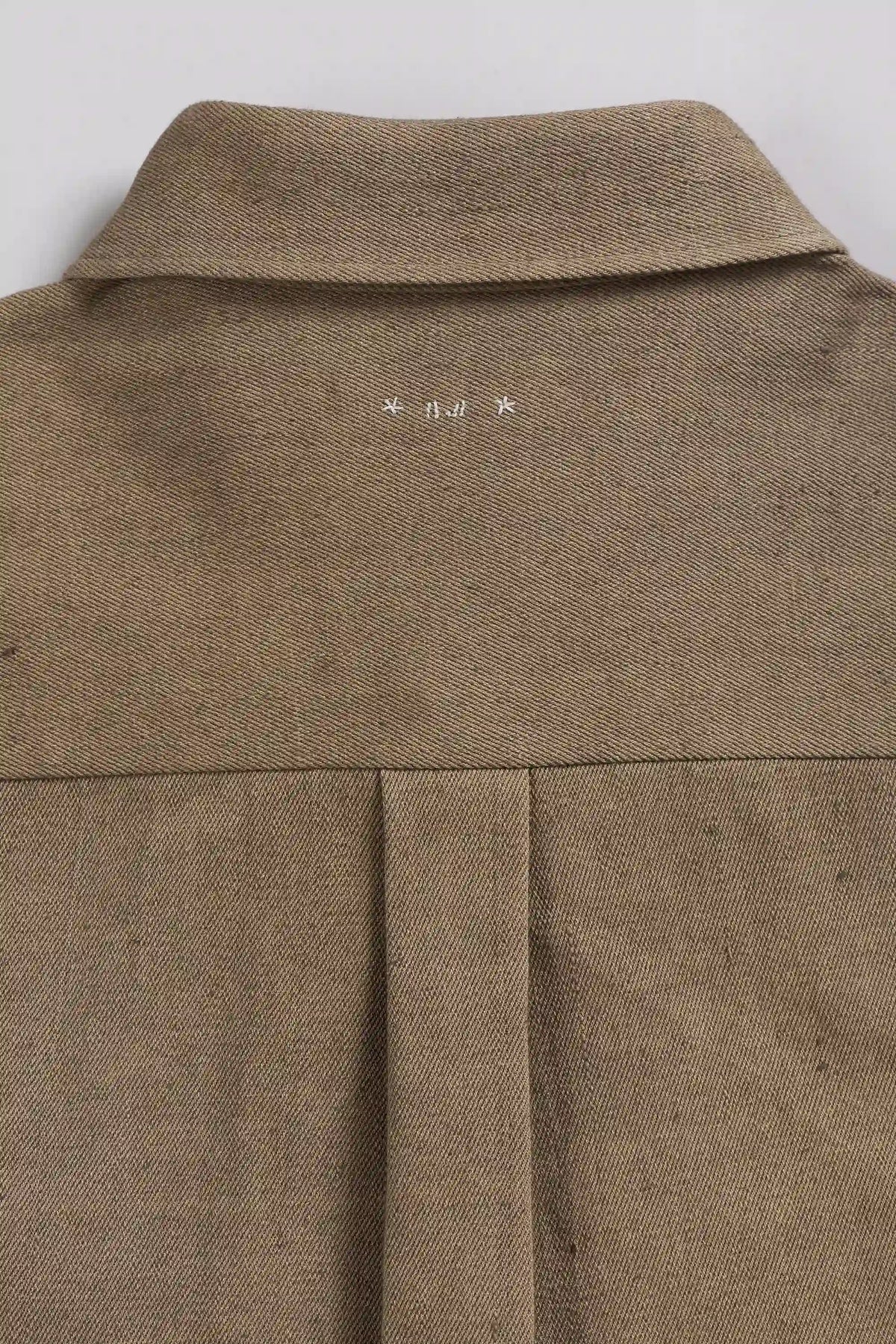 Close-up of the back collar and upper back of a brown, showing a small white printed logo centered below the collar.
