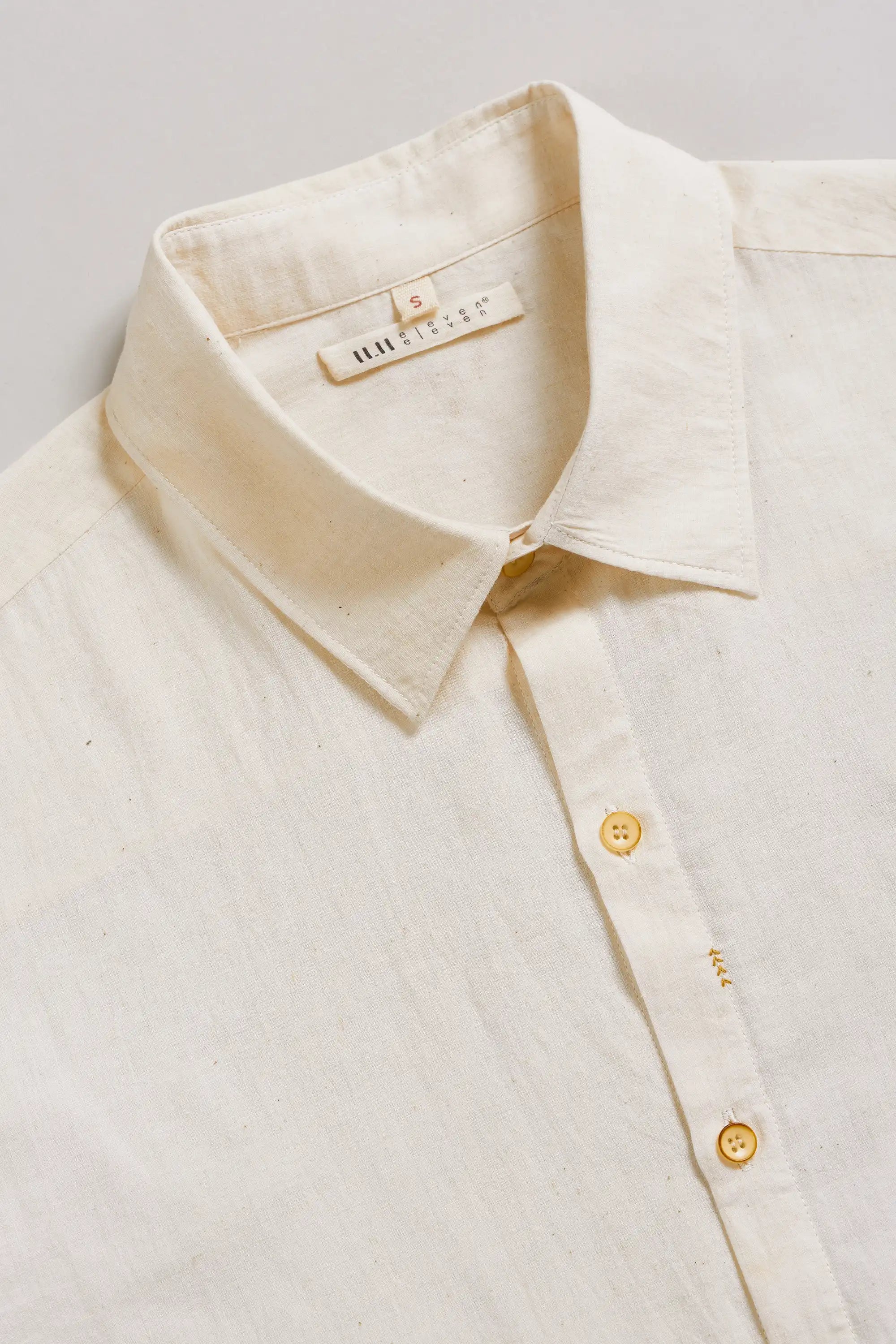 Close-up of a cream-colored shirt with a collar and buttons on a light grey background