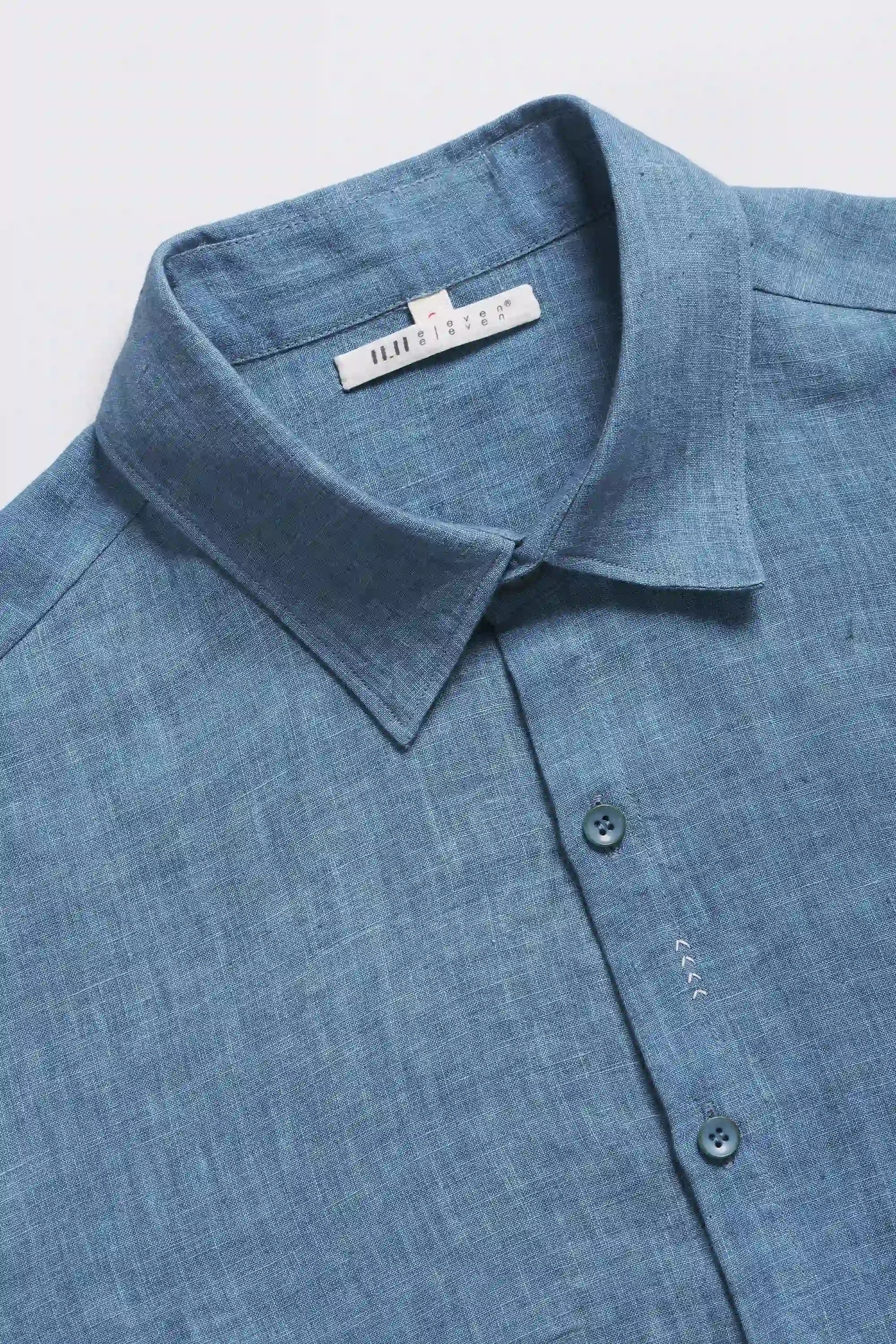 Close-up shot of a blue shirt with collar and buttons on a light grey background