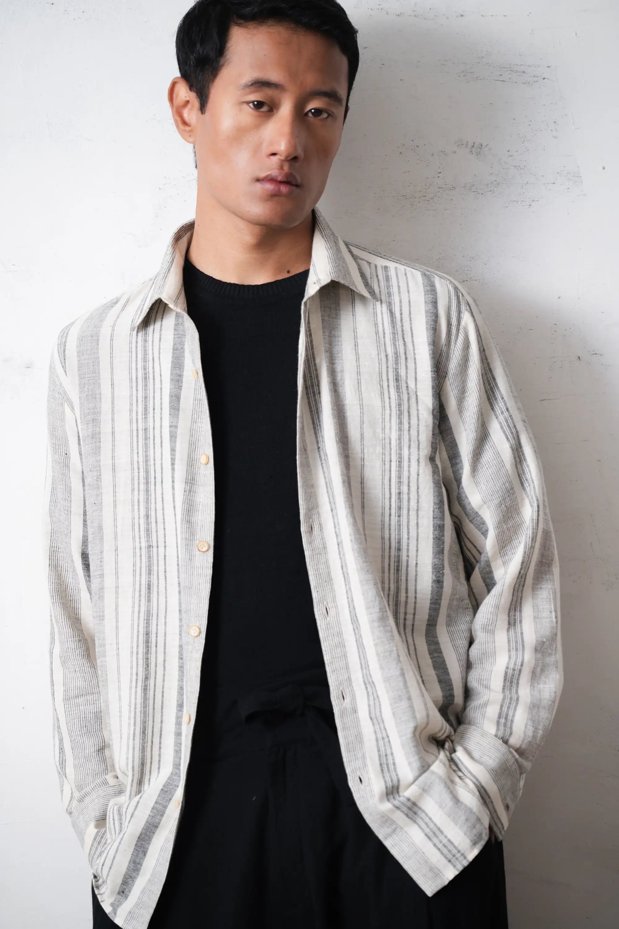 Man wearing a striped shirt over a black t-shirt on a light grey background