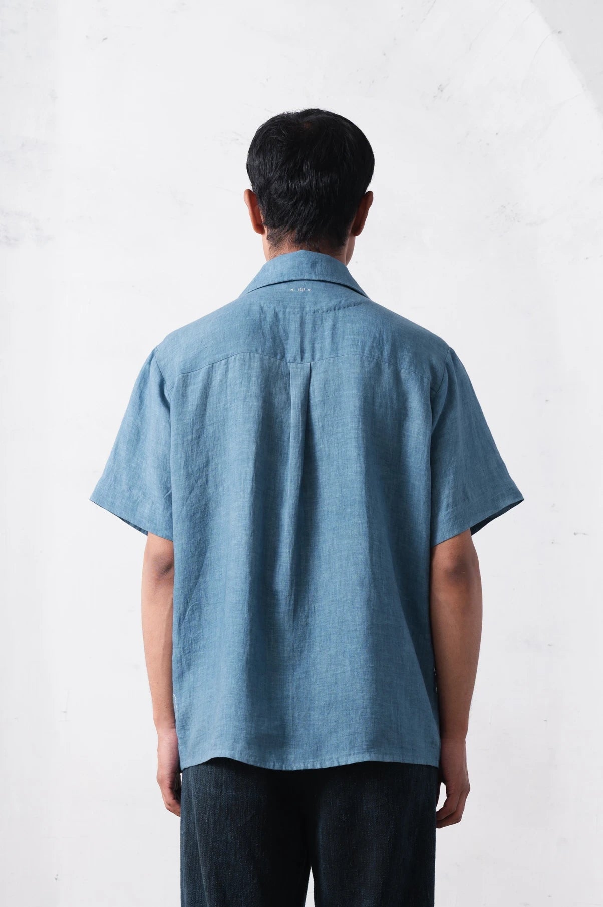 Back shot of a person wearing a blue shirt on a light grey background