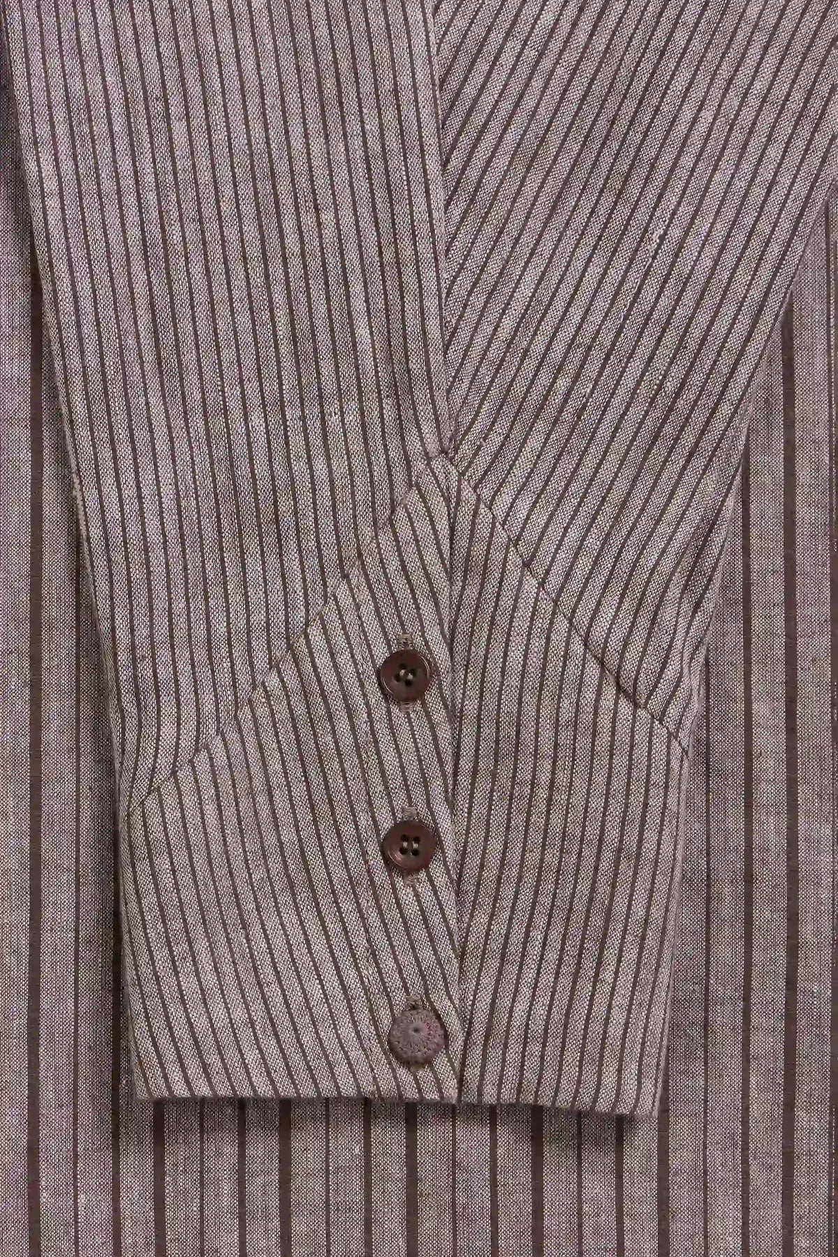 Close-up of a shirt sleeve with brown buttons on a taupe-grey and brown vertically striped fabric.