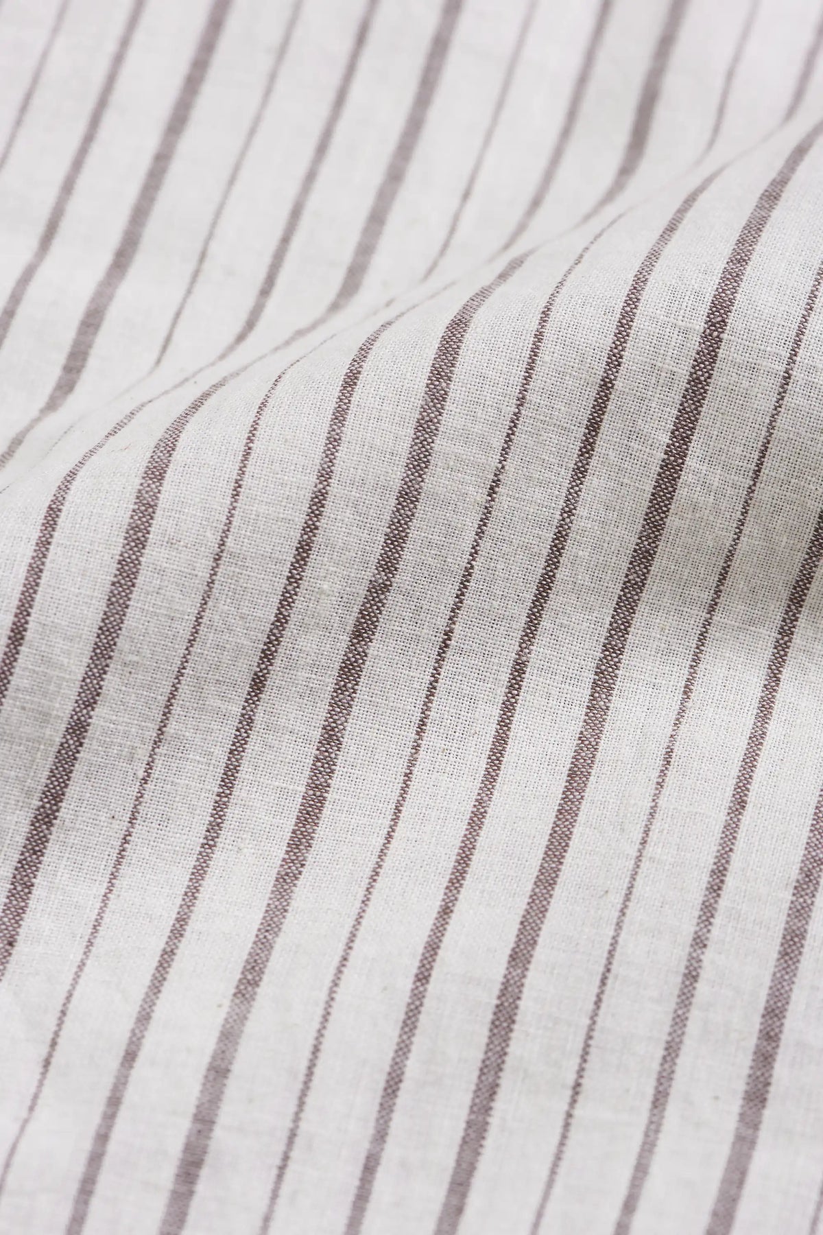 A close-up of a textured fabric with vertical brown stripes on a warm off-white fabric.