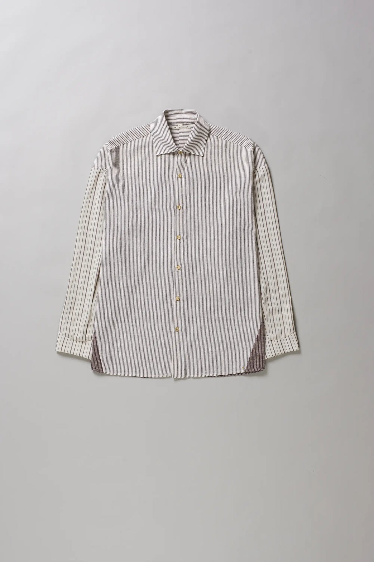 A ecru cotton button-up shirt with vertical stripes on the sleeves and a subtle brown textured panel lining the hem and side pockets, displayed flat against a neutral grey background.