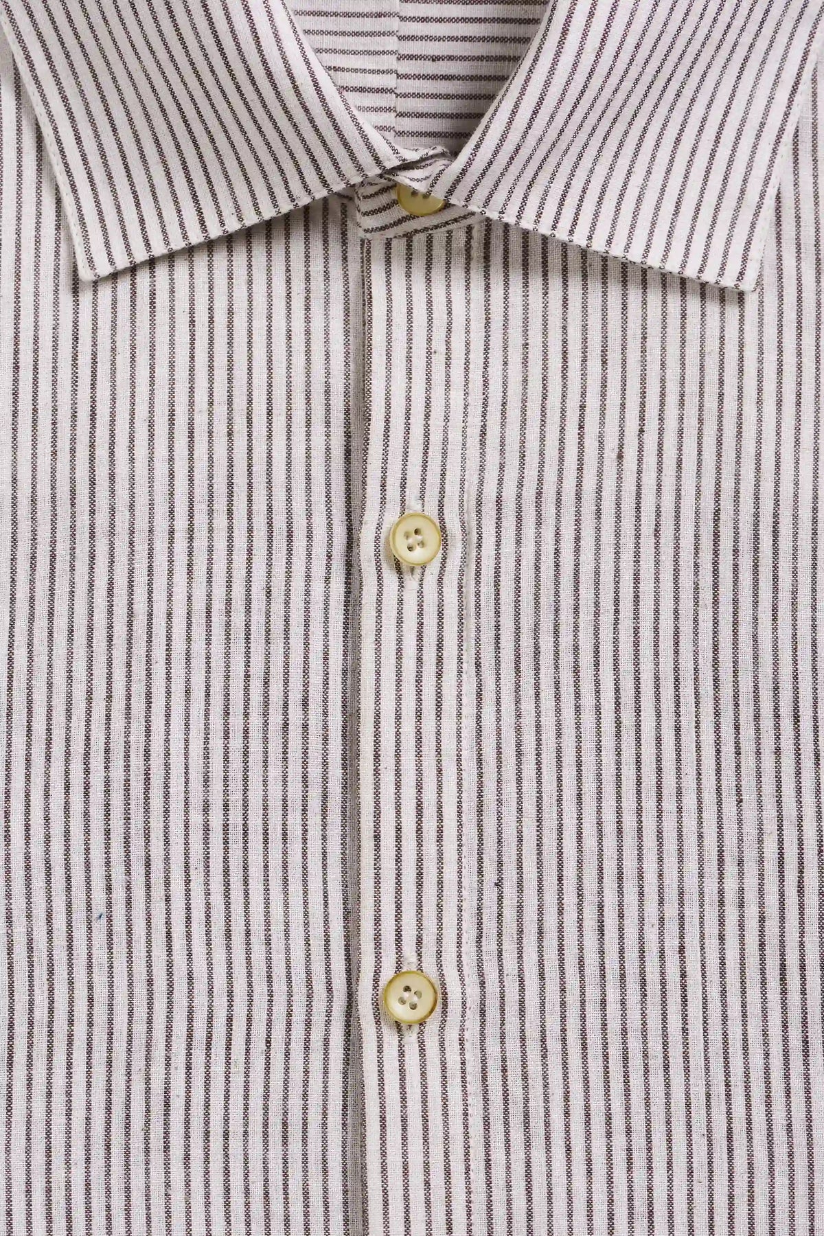 Close-up of a collared button-down shirt with thin vertical dark stripes on a light beige or off-white base, featuring three visible buttons.