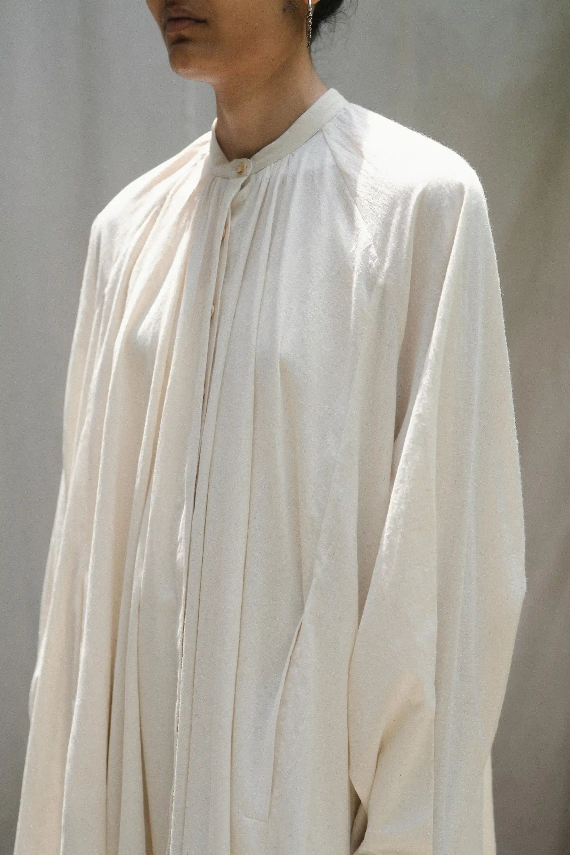 Person wearing a ecru long-sleeve shirt against a plain background