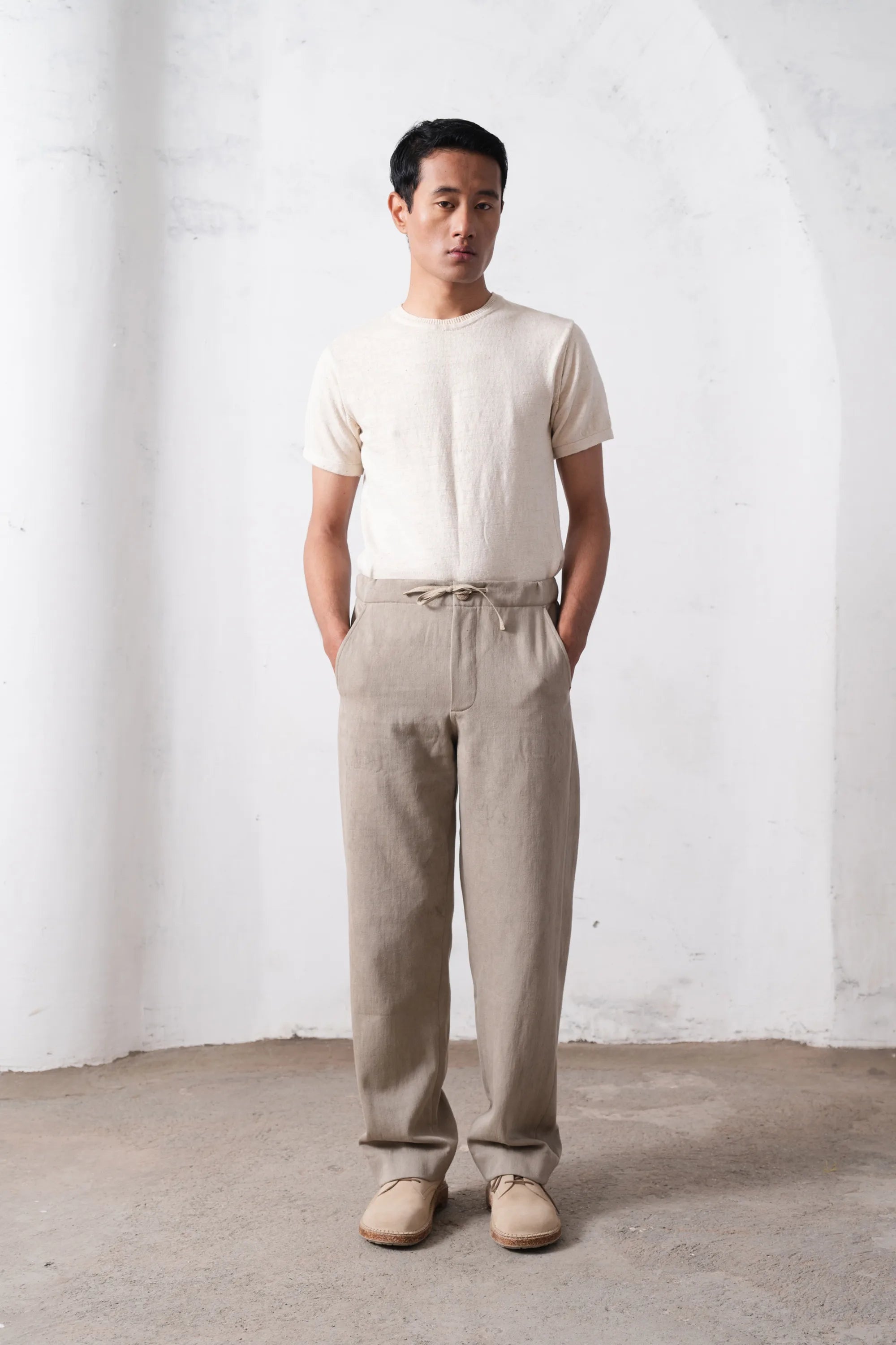 Man wearing a t-shirt and pants standing against a light grey wall