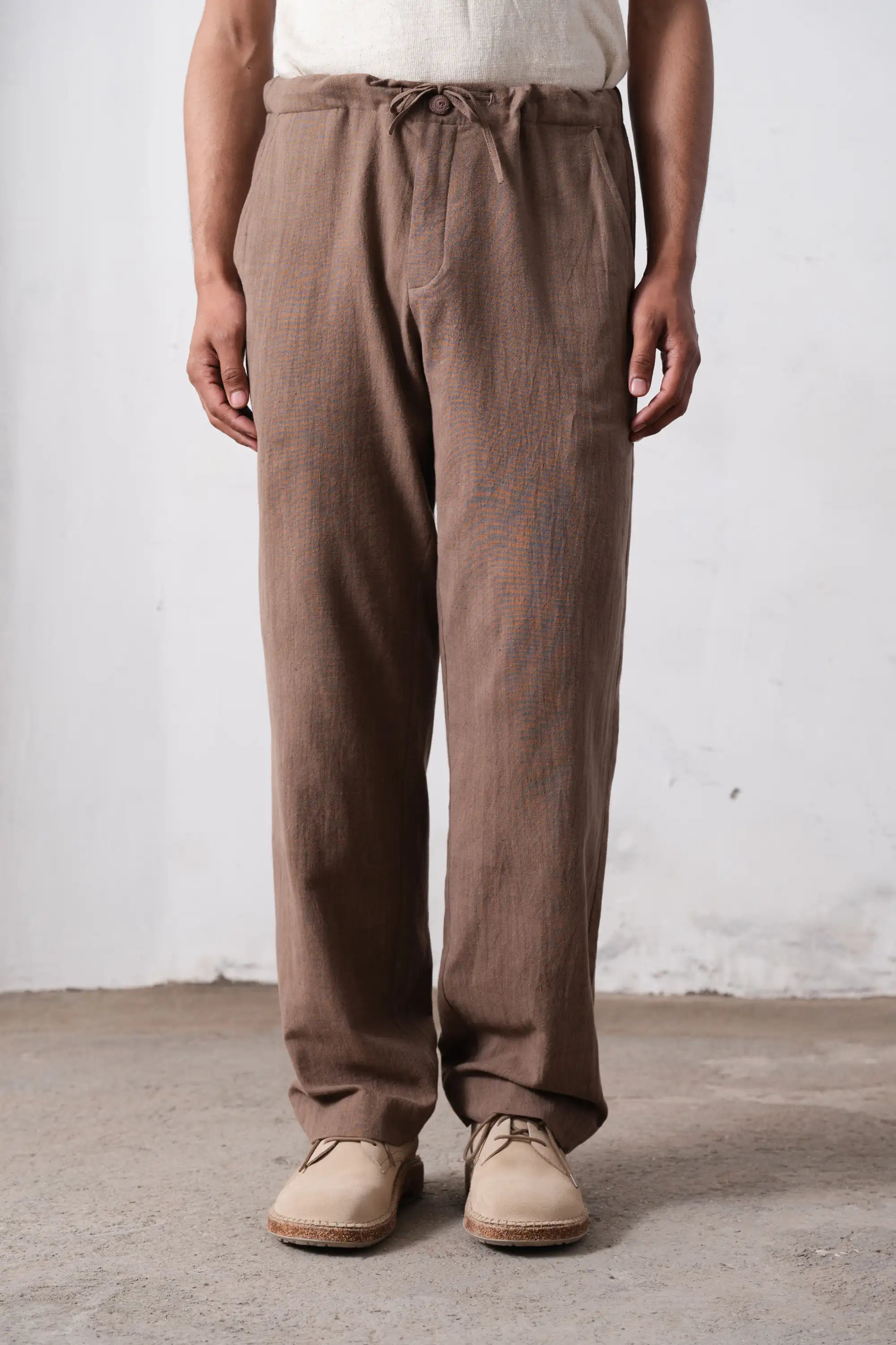 Person wearing brown pants standing against a light grey wall
